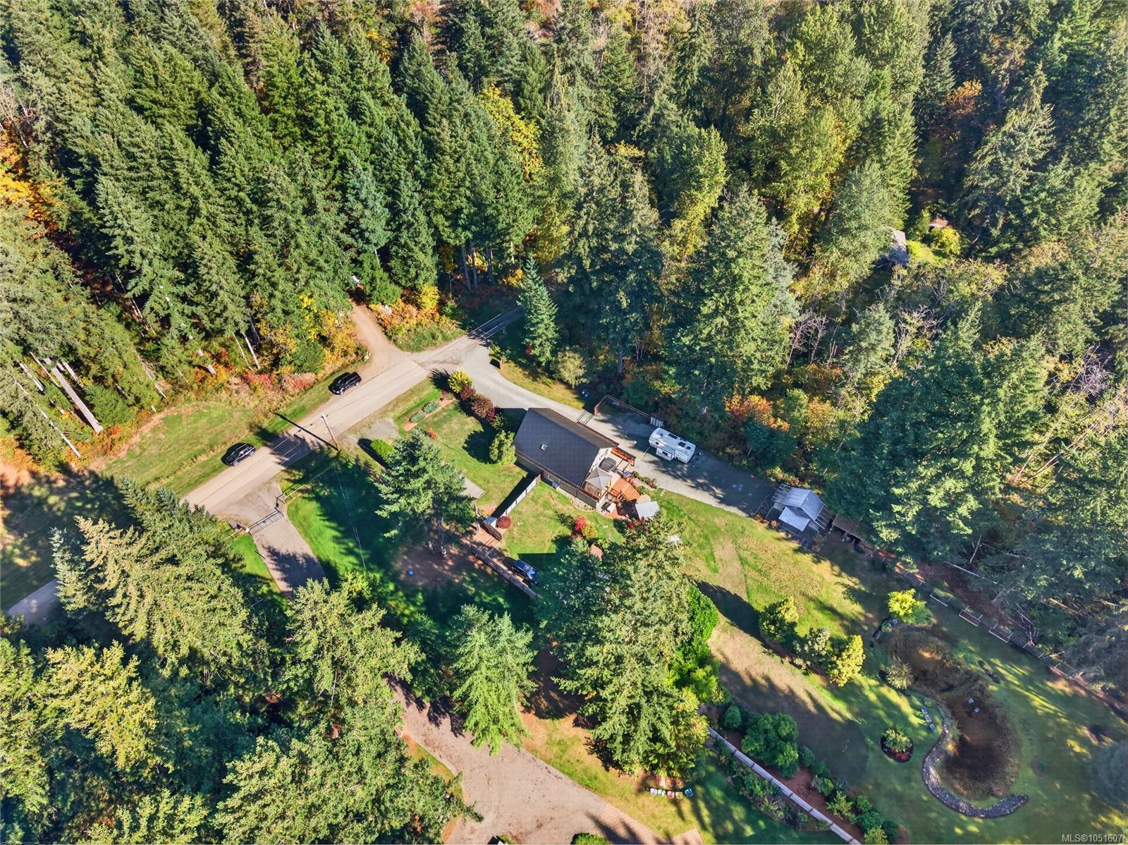 Aerial view of a home and yard bordered by dense forest, with a road and RV nearby.