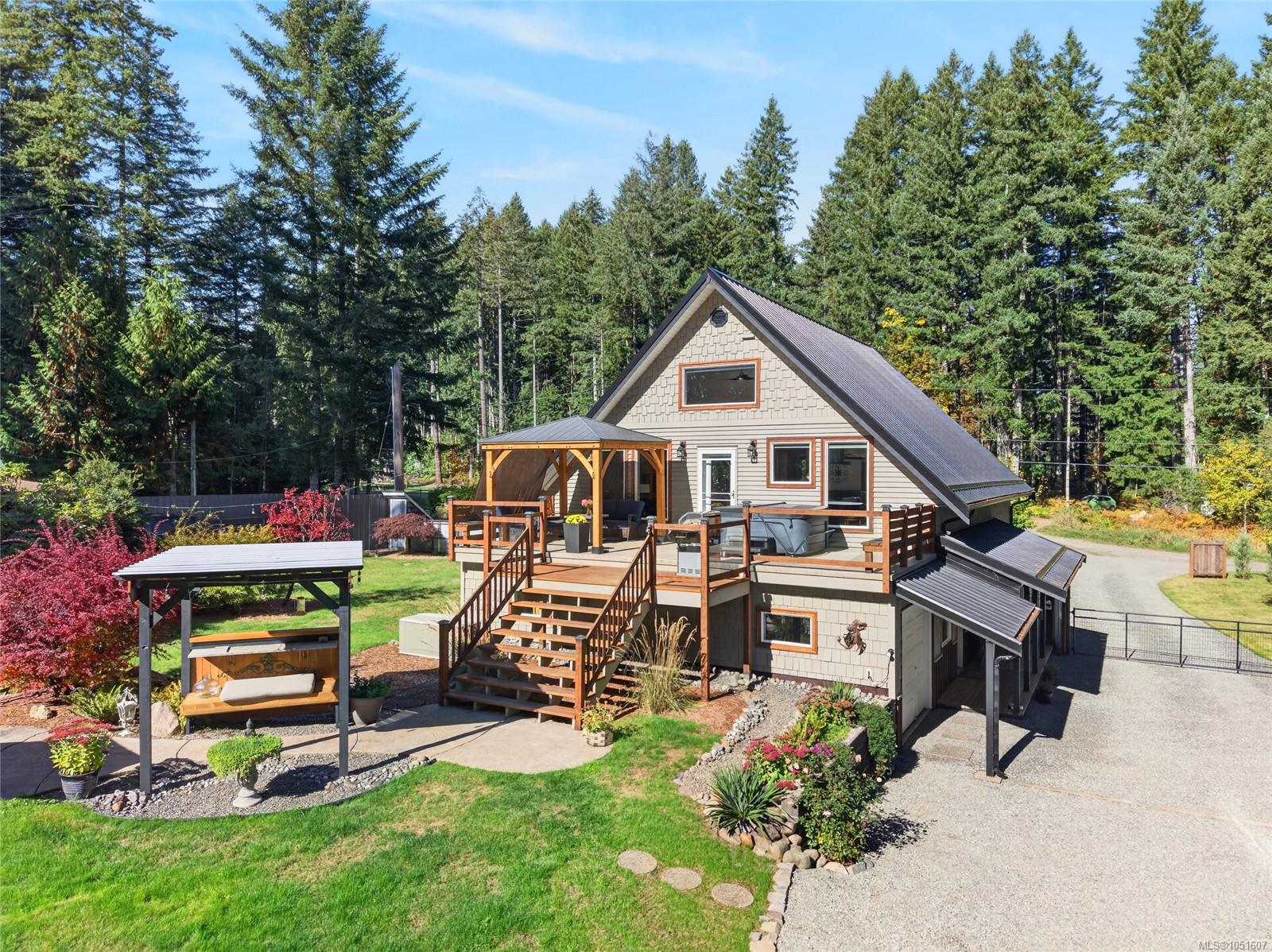 A-frame house with a broad wooden deck, covered seating, and hot tub in a wooded setting.