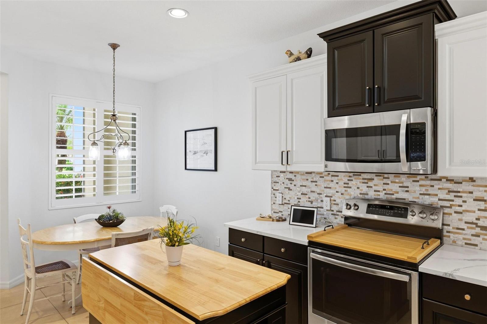 Kitchen with dark cabinets, a butcher-block island, and a dining nook beside shuttered windows.
