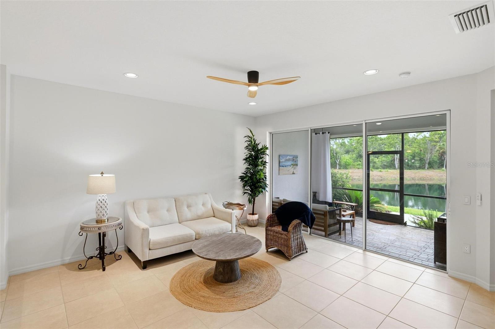 Living room with a white sofa and sliding glass doors opening to a screened patio overlooking a pond.