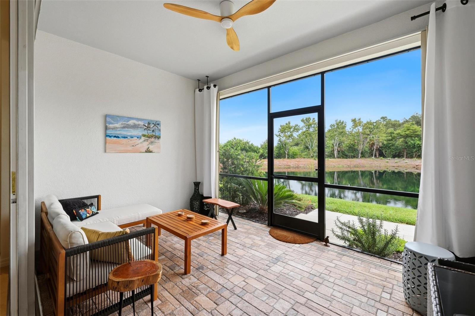 Furnished sunroom with a large screened window overlooking a pond and trees.