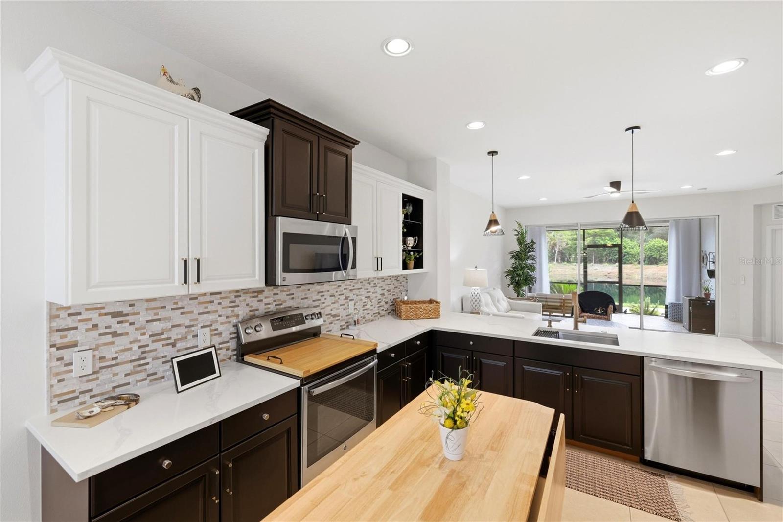 Kitchen with dark cabinets, white counters, stainless appliances, and an island dining table opening to the living room.