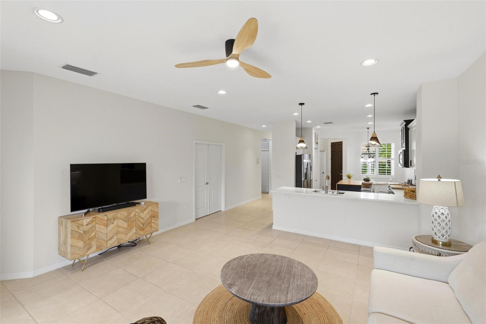 Open living room with tiled floors, a wood media console, and kitchen beyond.