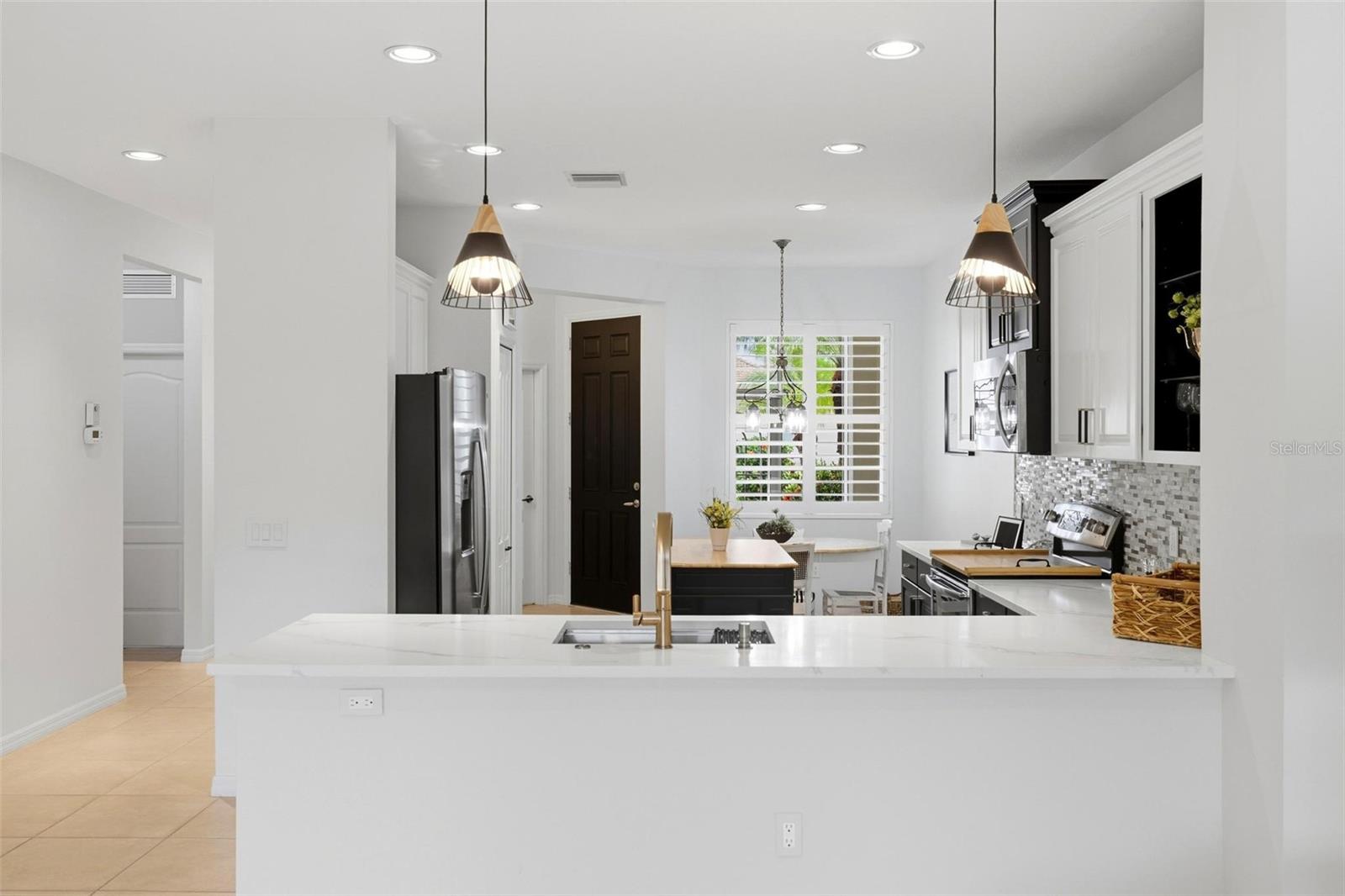 Bright kitchen with a large white island, stainless steel appliances, and mosaic tile backsplash.