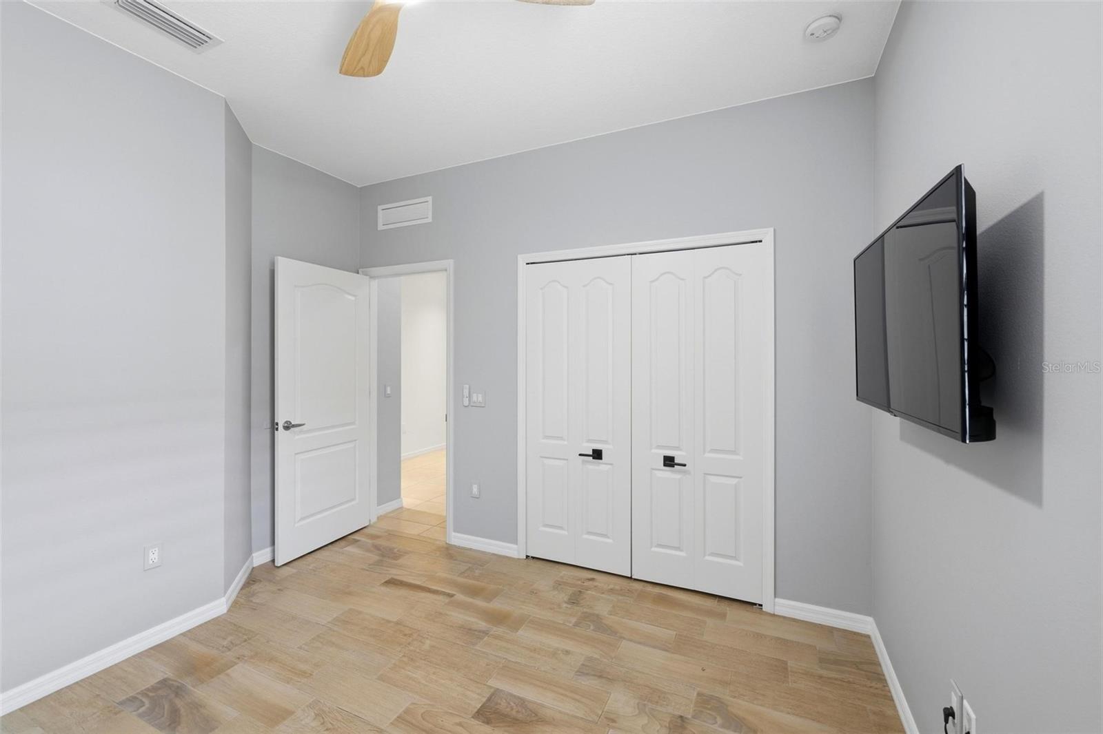 Empty room with a wall-mounted television, double closet doors, and light wood-look flooring.