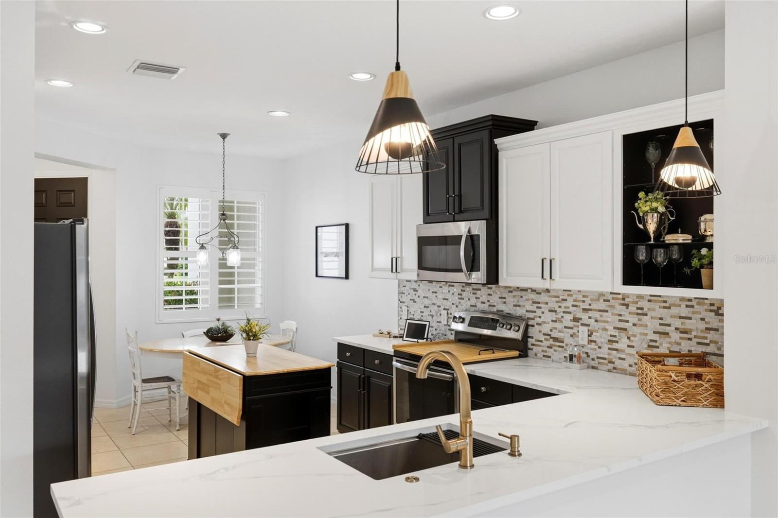 Kitchen with black and white cabinets, a mosaic backsplash, and a broad marble island.
