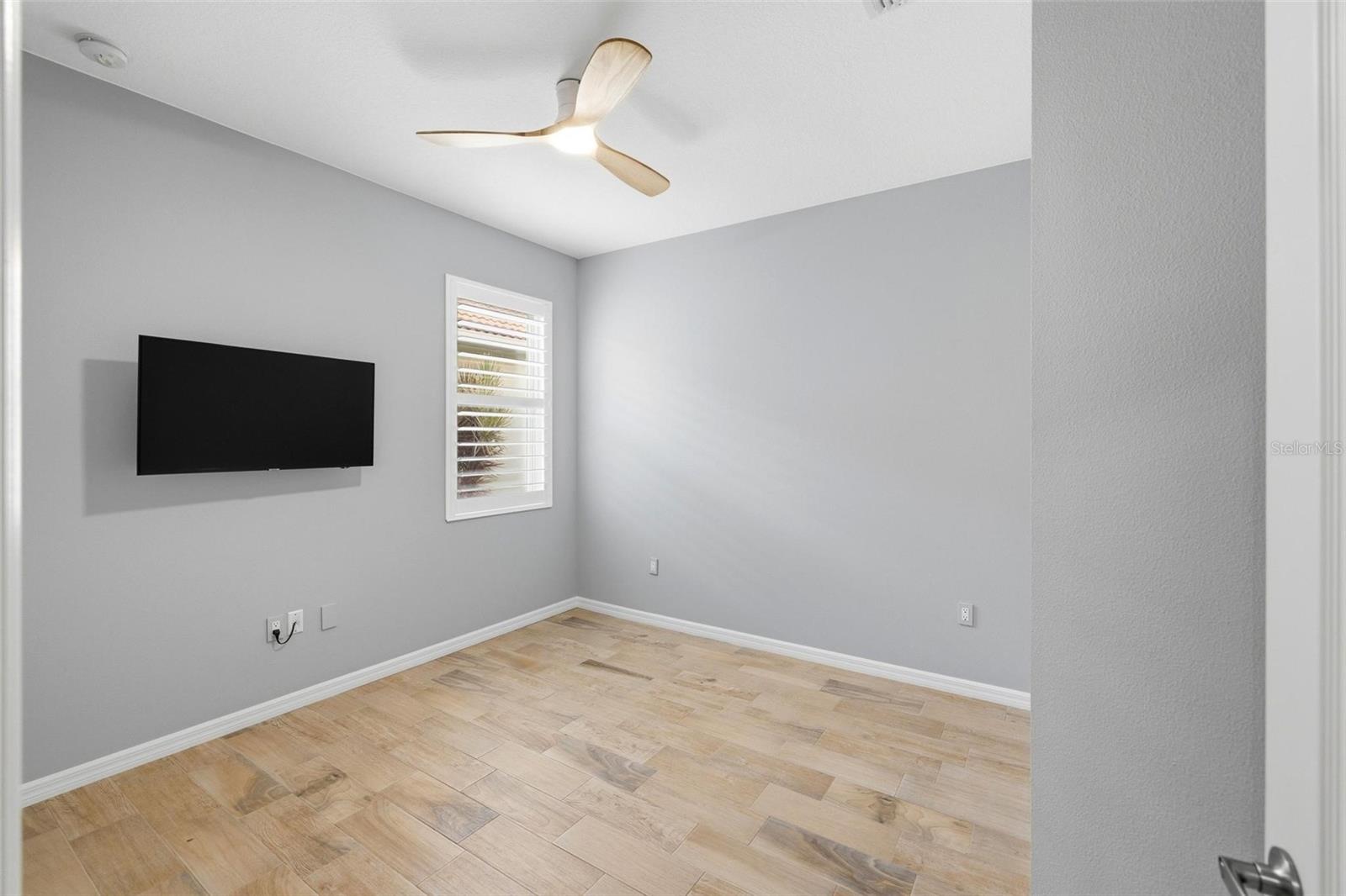 Interior room with light wood-look tile, gray walls, a wall-mounted TV, and ceiling fan.