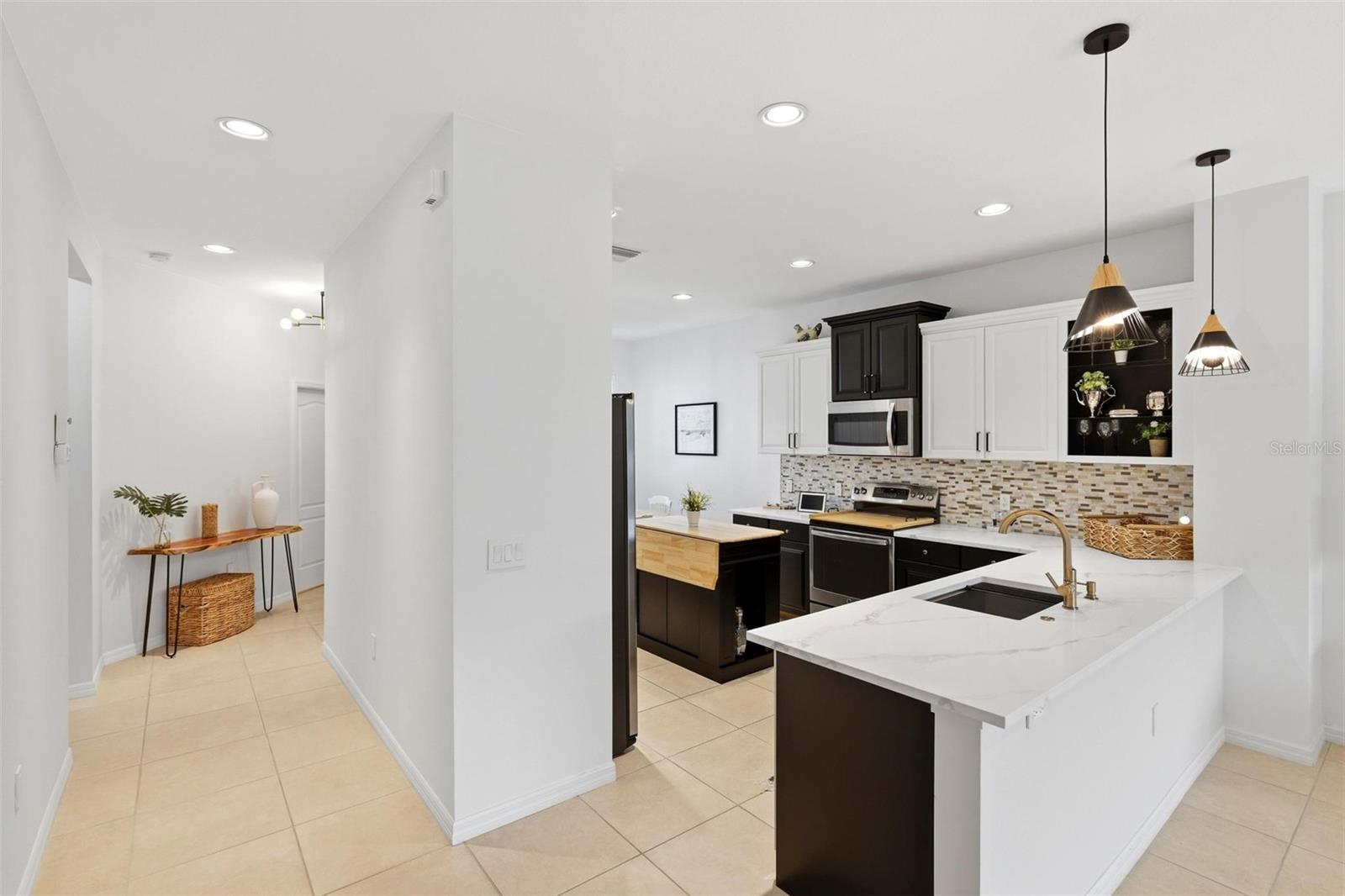 Bright kitchen with a marble-look island, dark cabinets, mosaic backsplash, and pendant lights.