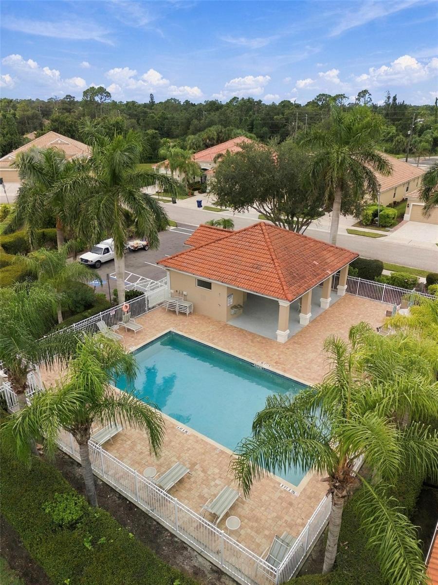 Aerial view of a fenced community pool, tile-roofed pavilion, and palm-lined deck.
