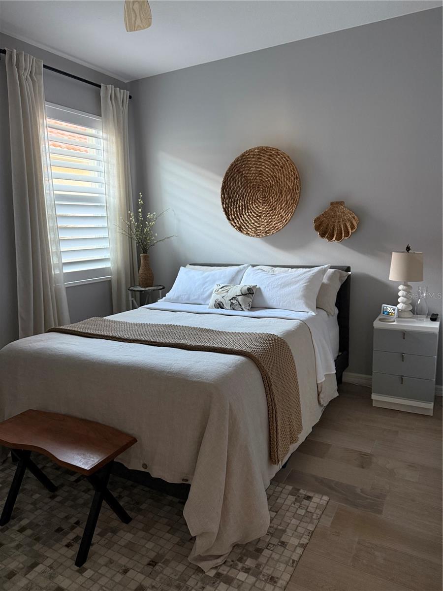 Bedroom with a white bed, woven wall decor, and plantation shutters.