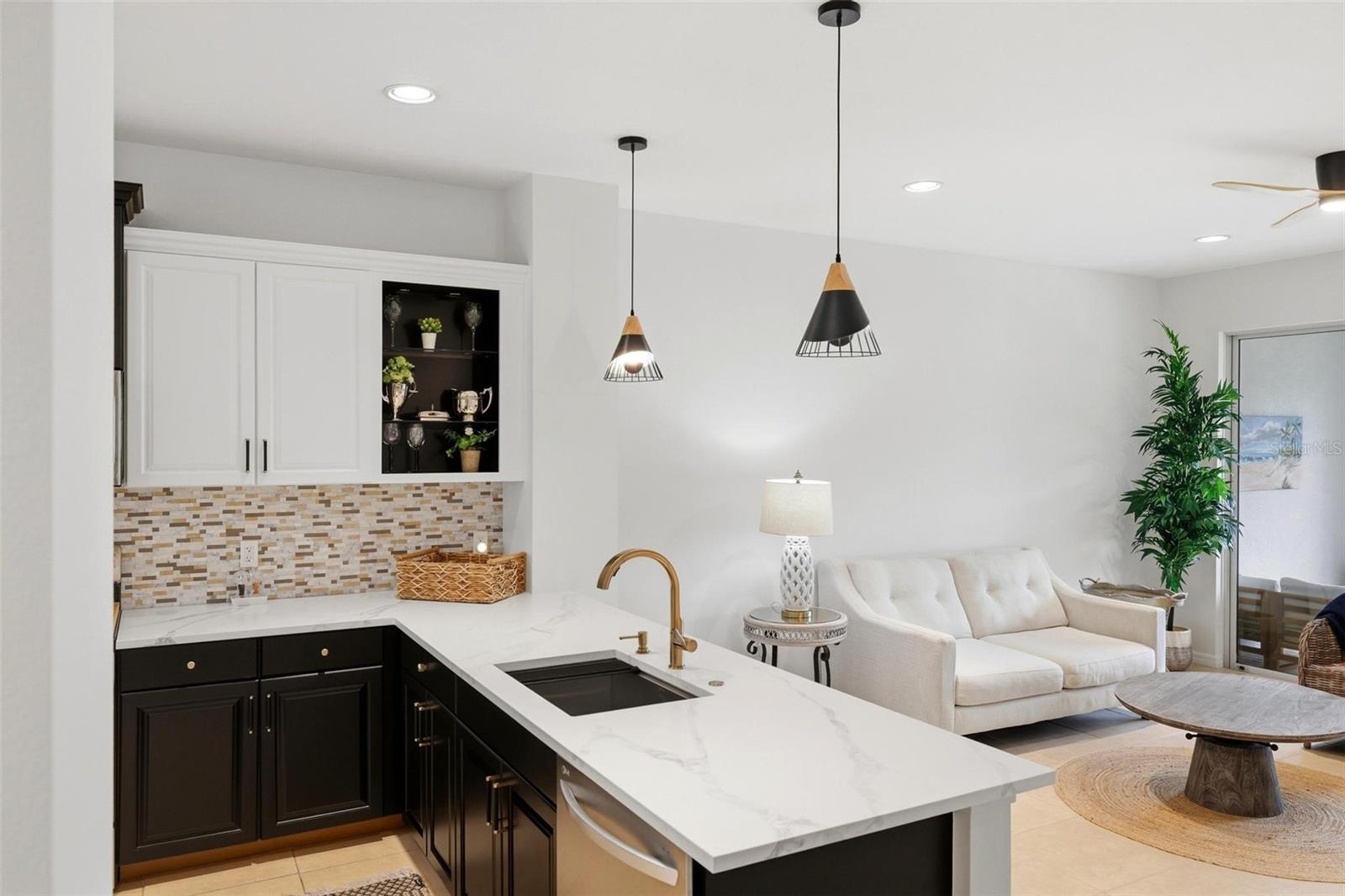 Open kitchen and living area with a white marble island, dark cabinetry, and cream sofa.