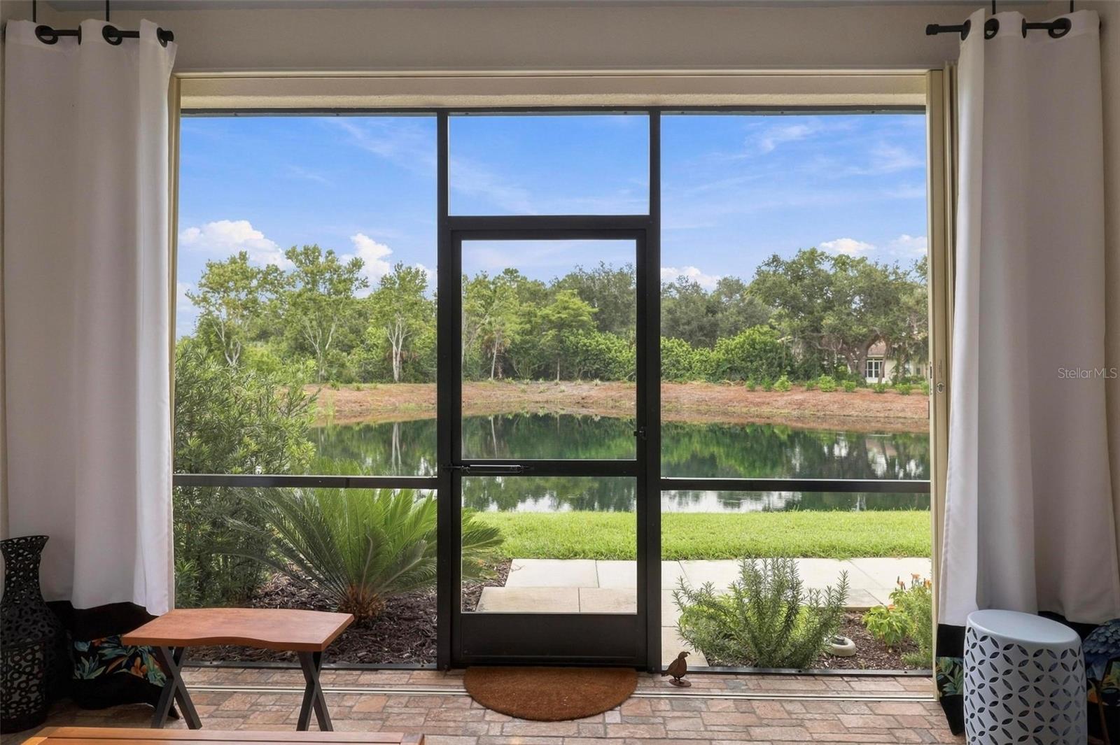 Sliding glass doors frame a pond view, with curtains and a tiled floor.