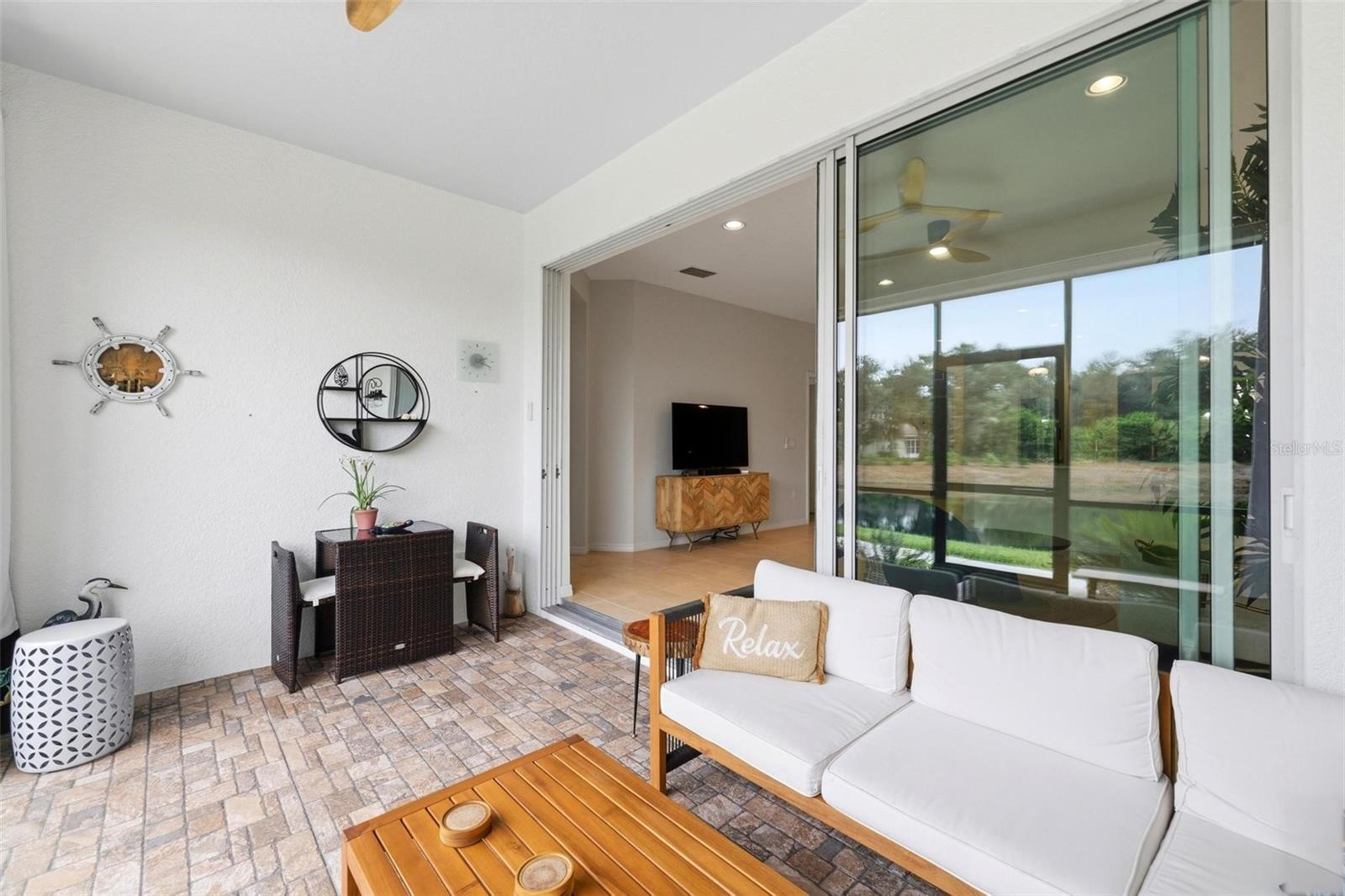 Covered patio with wicker dining set, cushioned sofa, and sliding doors opening to the living room.