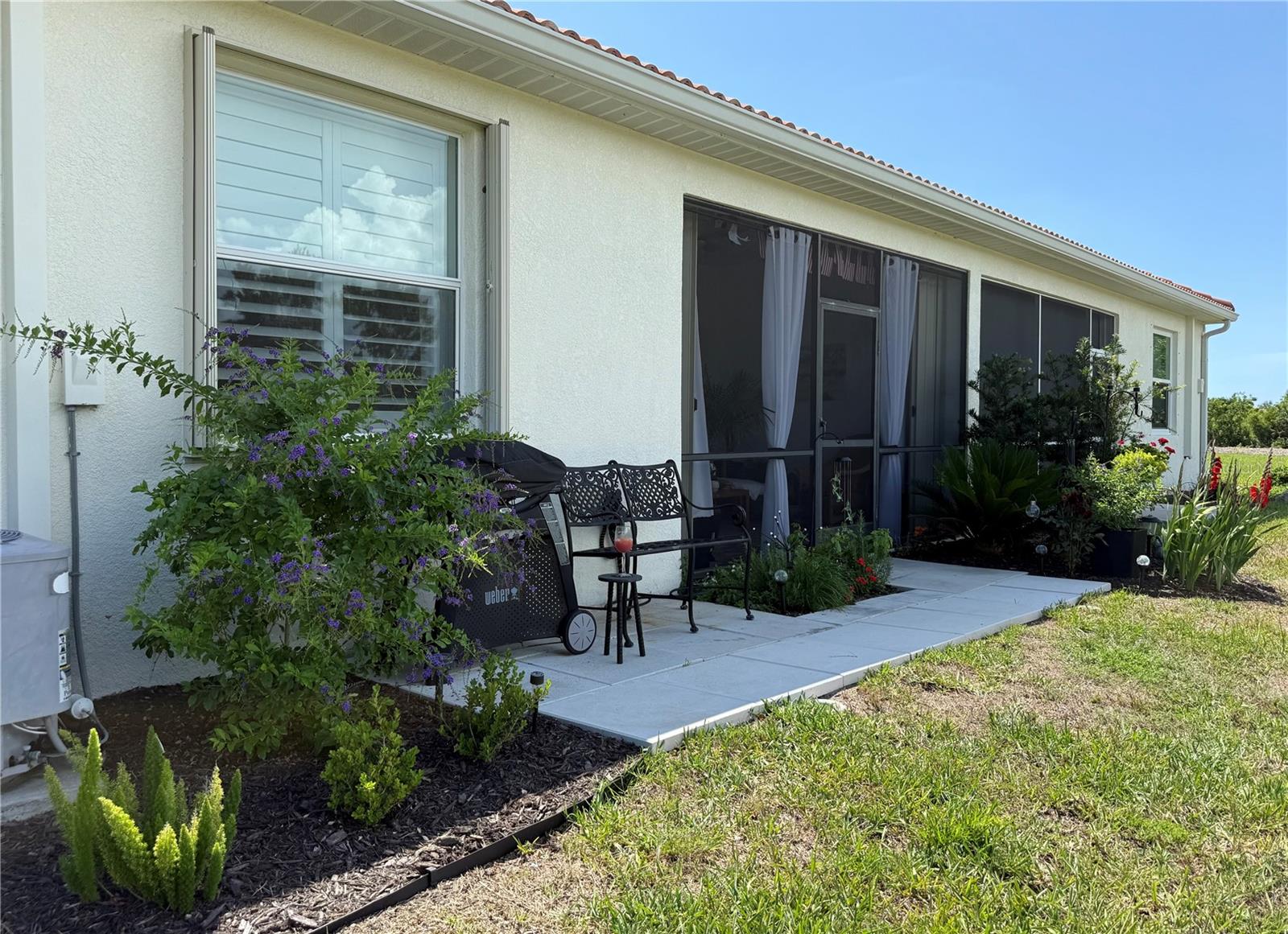 Home’s landscaped patio with a screened lanai, garden bench, and flowering shrubs.