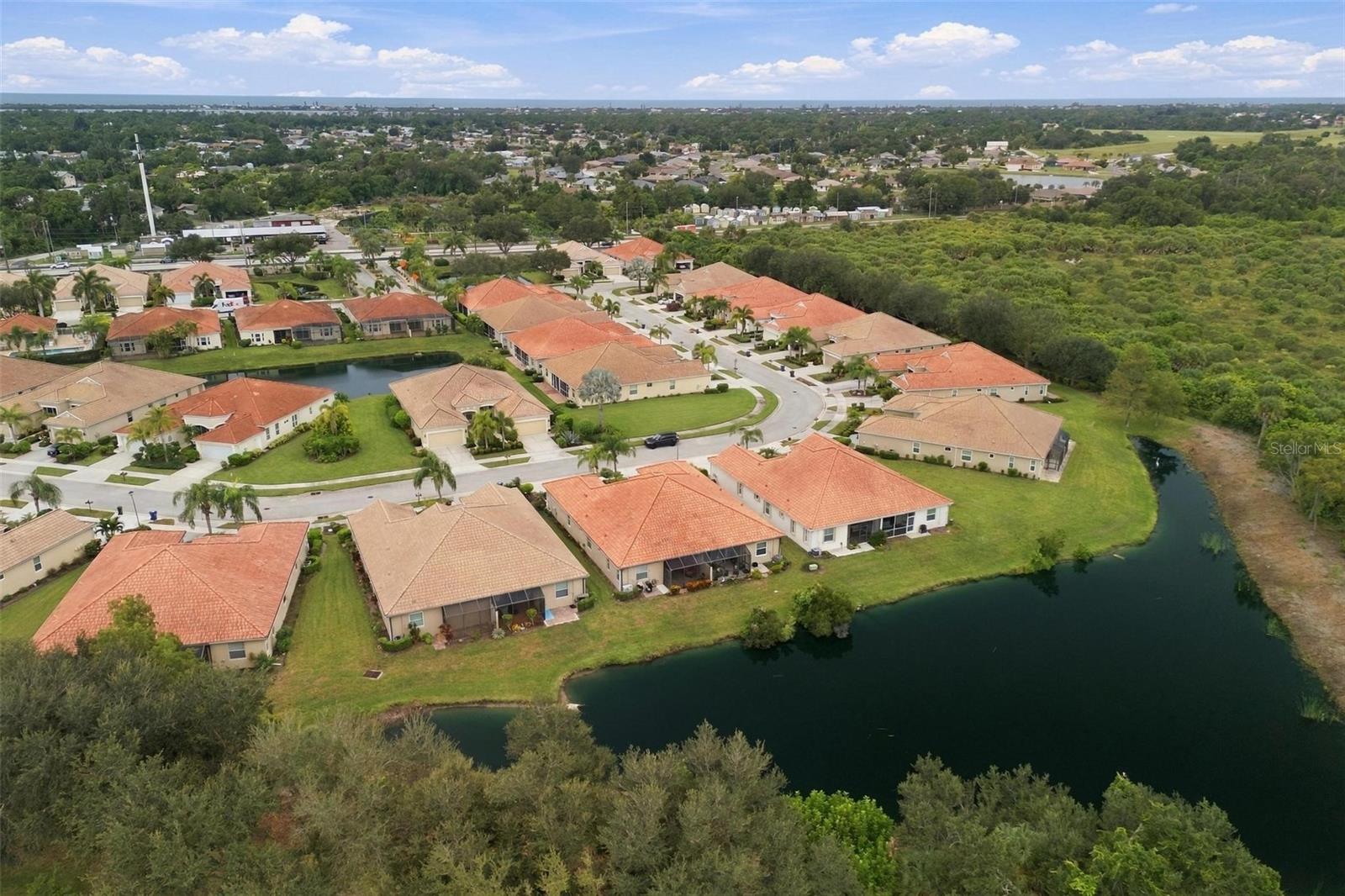 Aerial view of homes around a pond, with red tile roofs and surrounding green space.