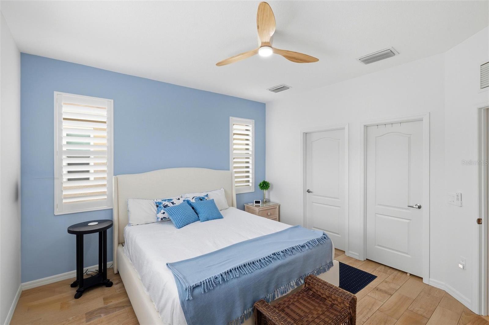 Bedroom with a white bed, blue accent wall, plantation shutters, and a wood-blade ceiling fan.