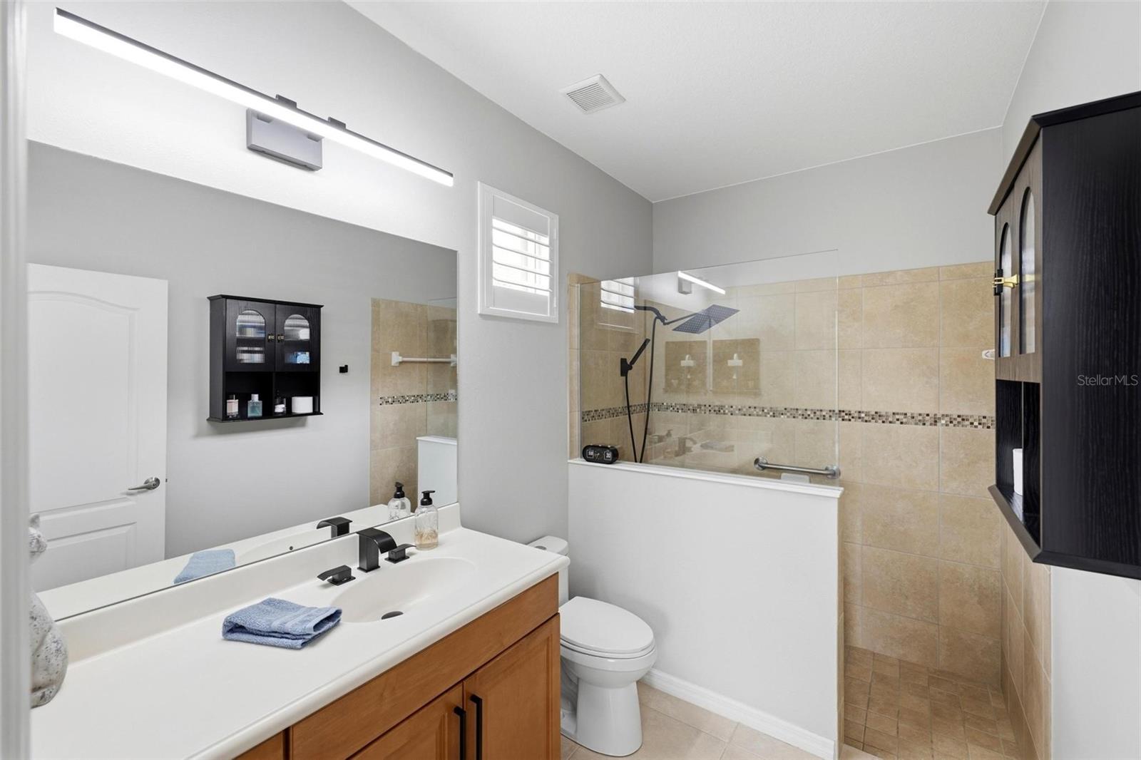 Bathroom with a double vanity and glass-enclosed tub-shower with beige tile.