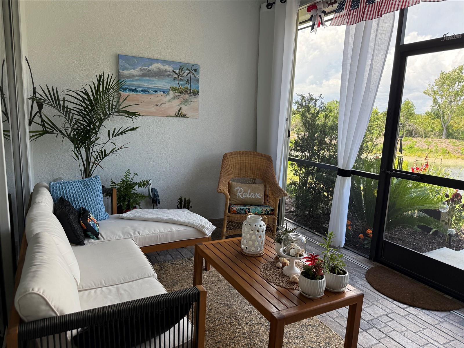 Screened lanai with wicker seating, a wooden coffee table, and garden views.