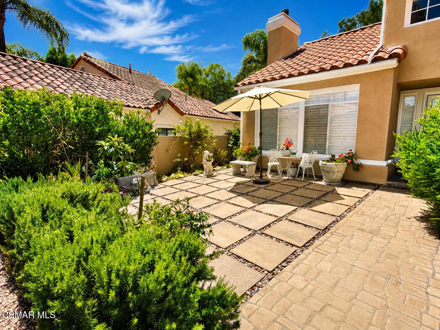 Landscaped home patio with a paver courtyard, outdoor dining set, and cream umbrella.