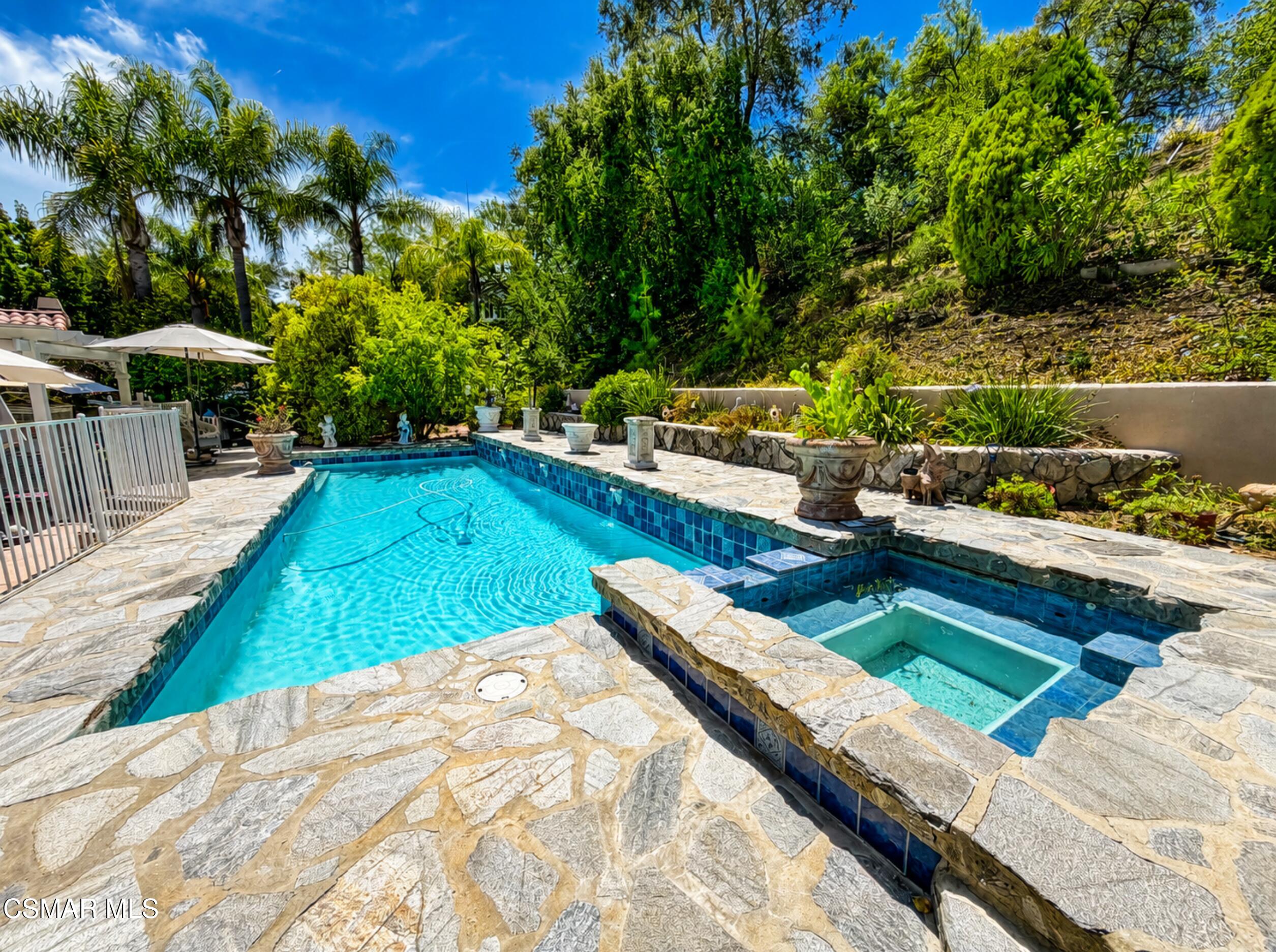 Outdoor swimming pool and attached spa with stone patio and lush landscaping.