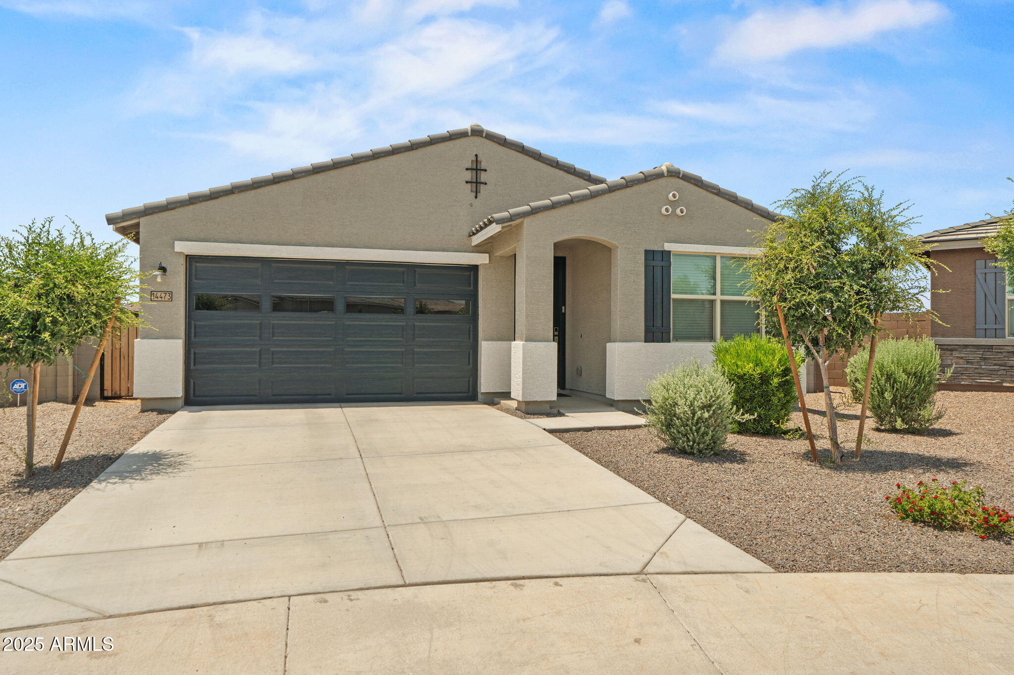 Single-story stucco home with a dark double garage door, recessed entry, and gravel desert landscaping.