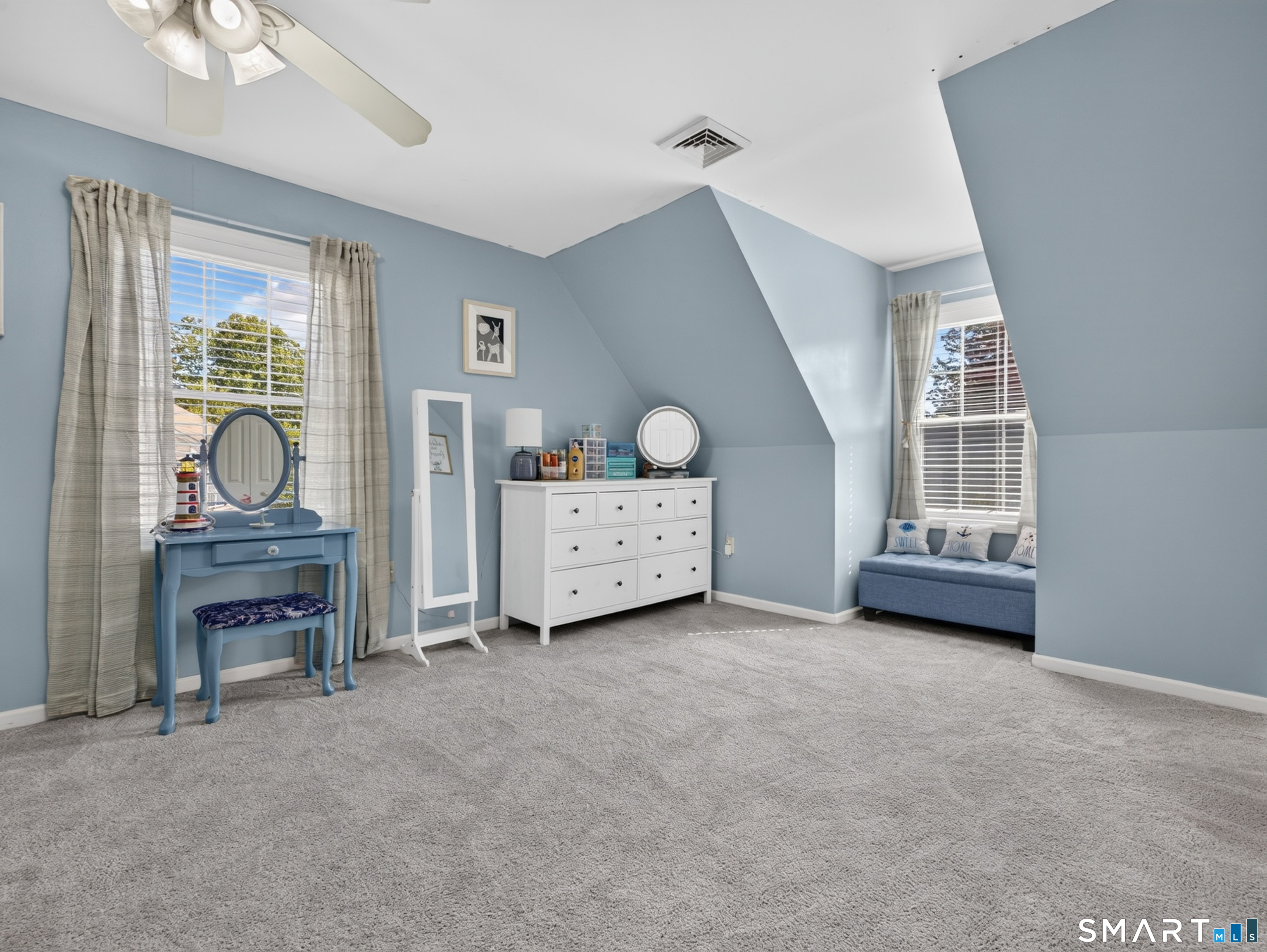 Bedroom with pale blue walls, gray carpet, a white dresser, and a window-seat nook.