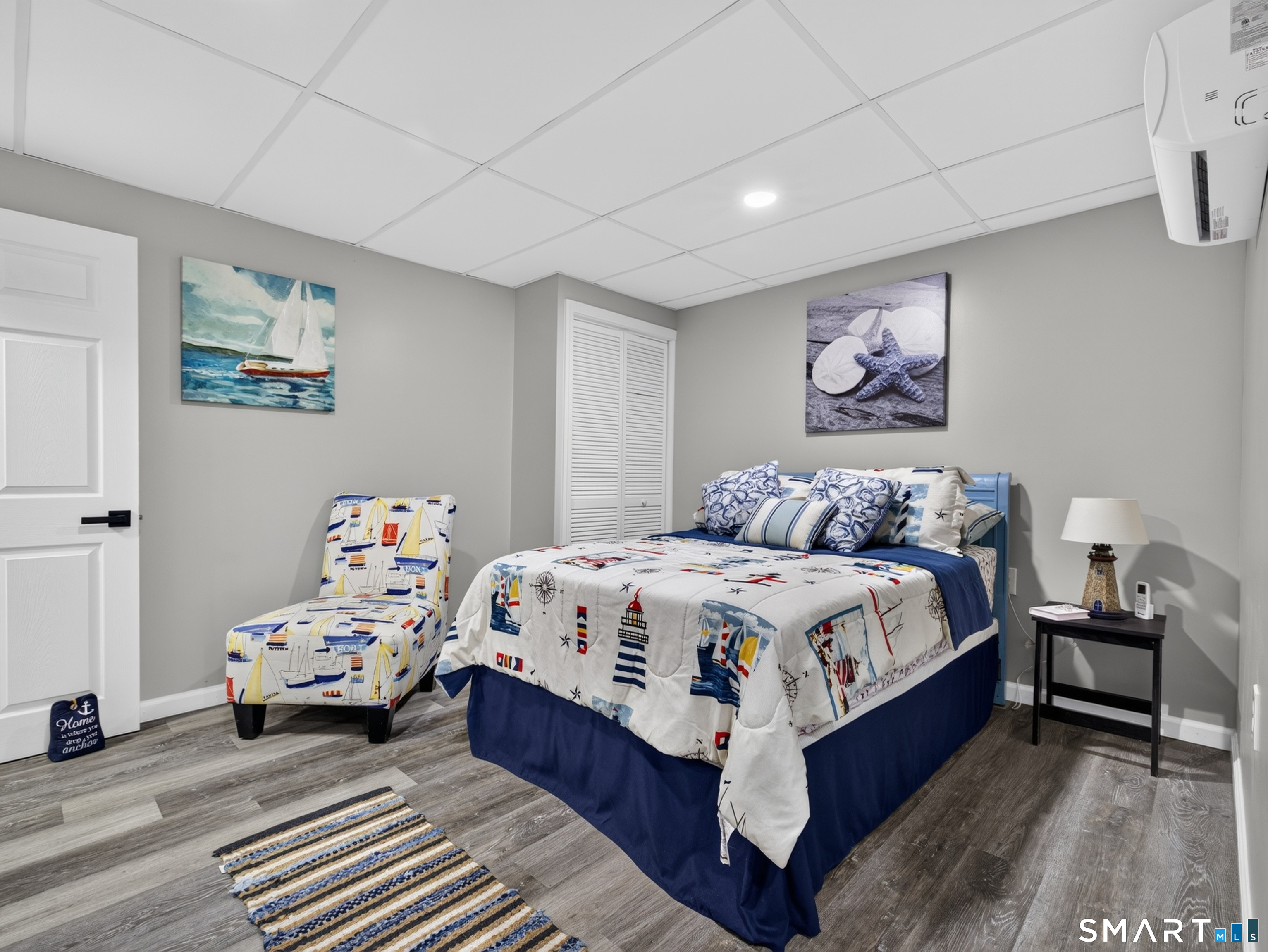 Nautical-themed bedroom with a blue bed, matching chair, and coastal artwork.