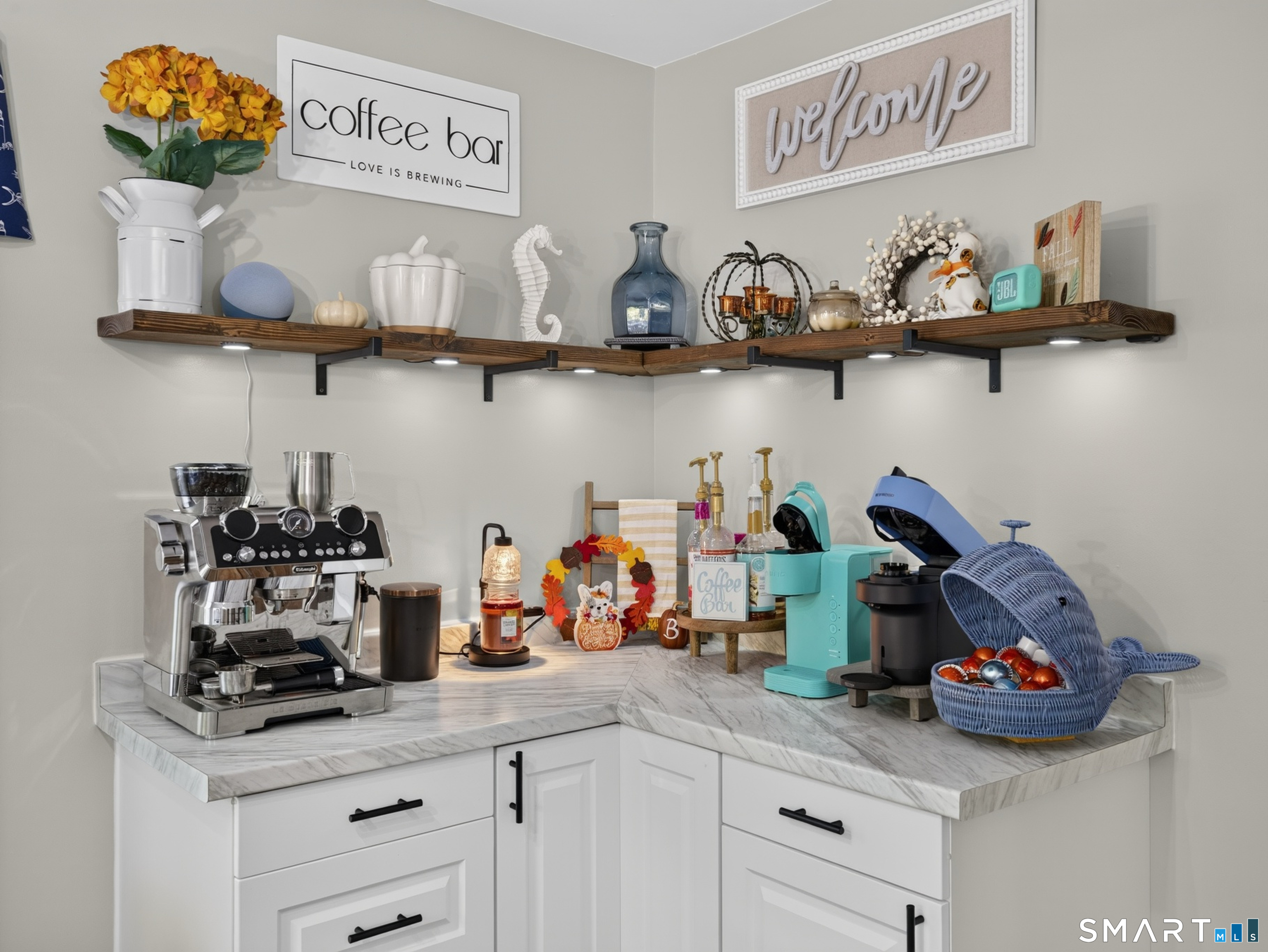 Coffee bar nook with espresso machines, marble counters, and decorative open shelving.