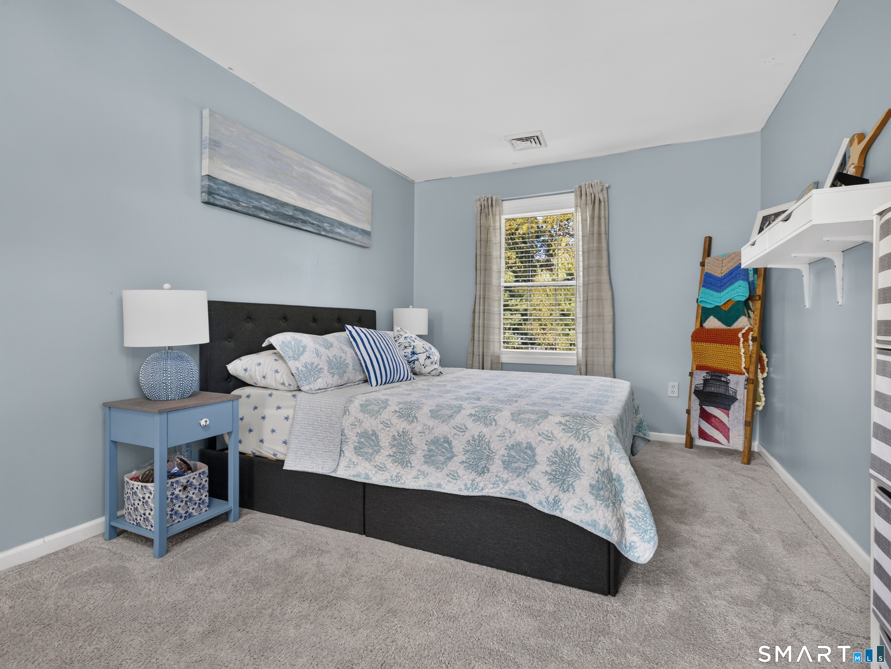 Furnished bedroom with a floral-covered bed, blue walls, and a window with plaid curtains.