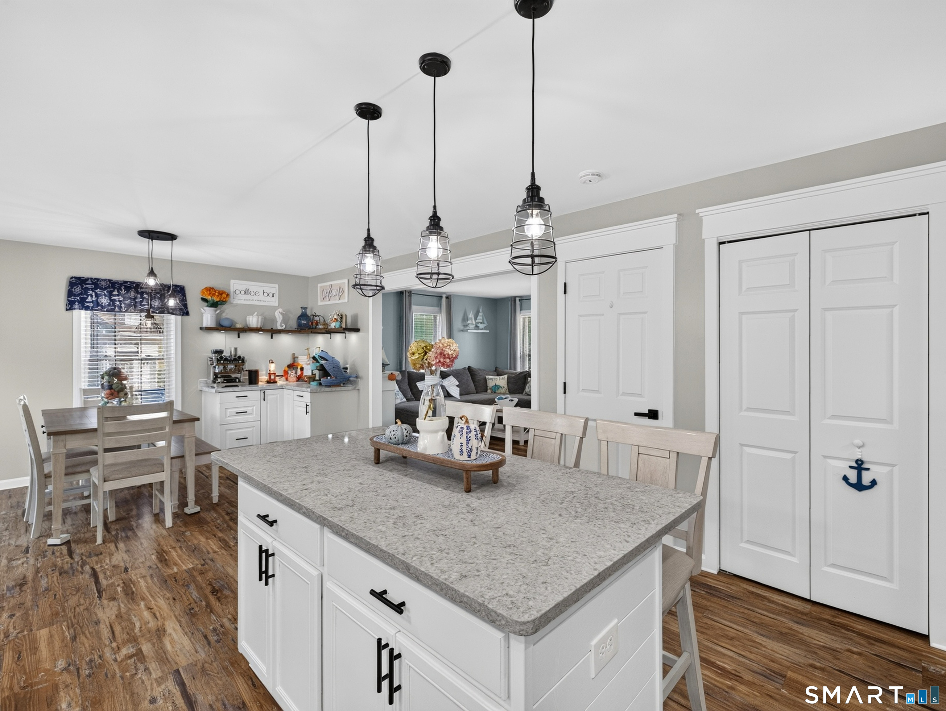 Bright kitchen with a large granite island, pendant lights, and dining area opening to the living room.