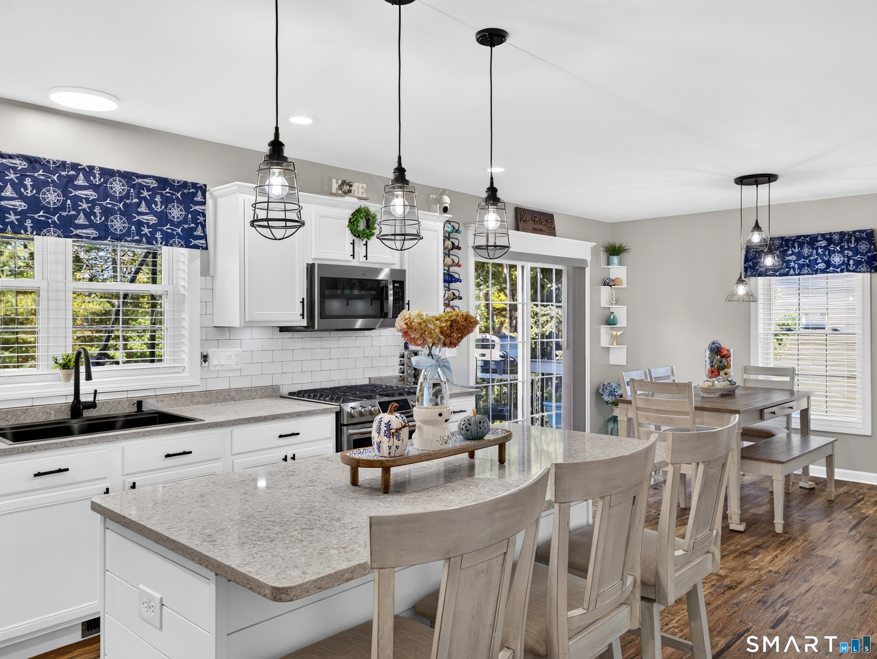 Bright kitchen and dining area with a large island, white cabinets, and nautical window valances.