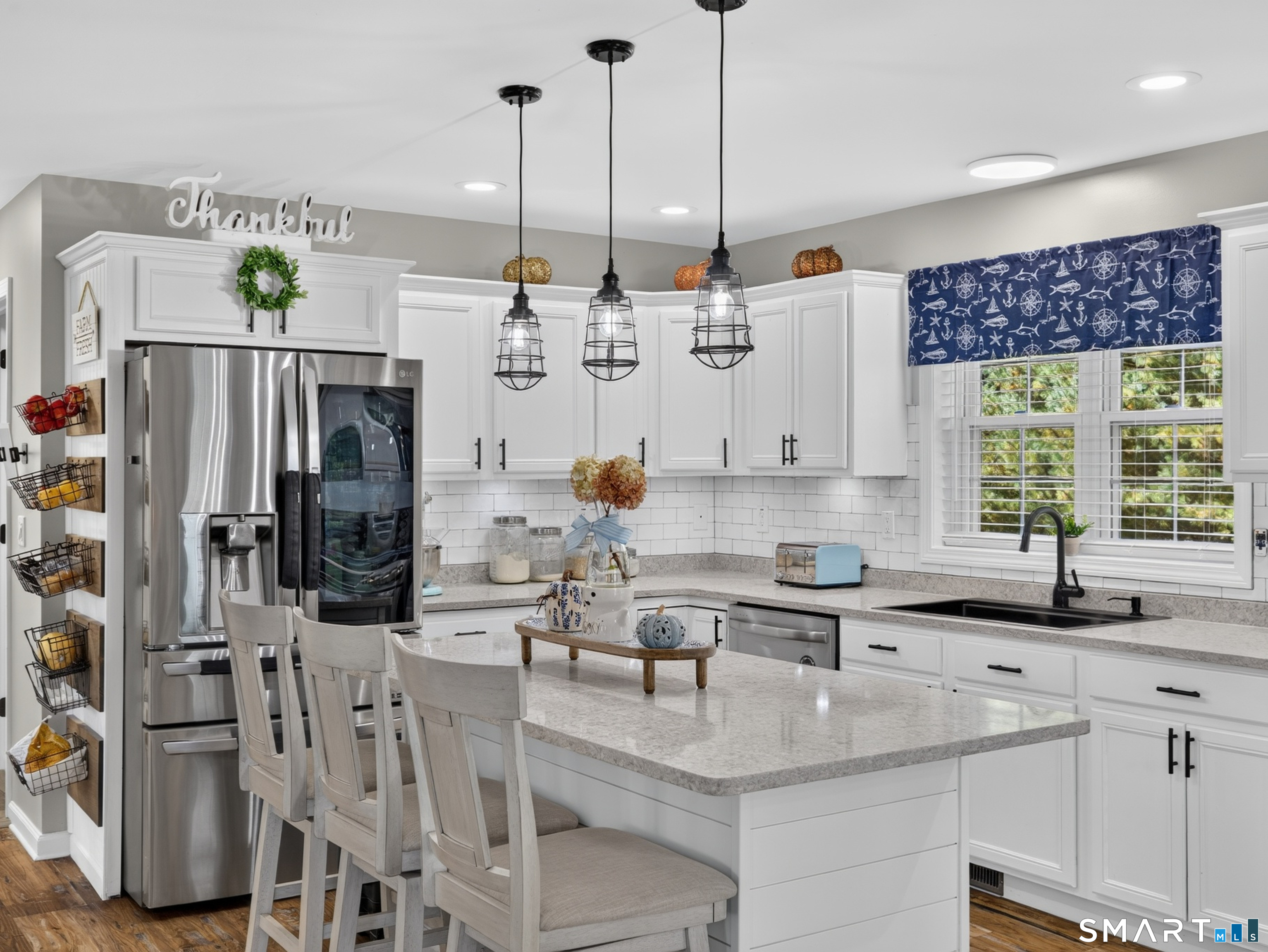 Bright white kitchen with a large island, stainless steel refrigerator, and navy nautical window valance.