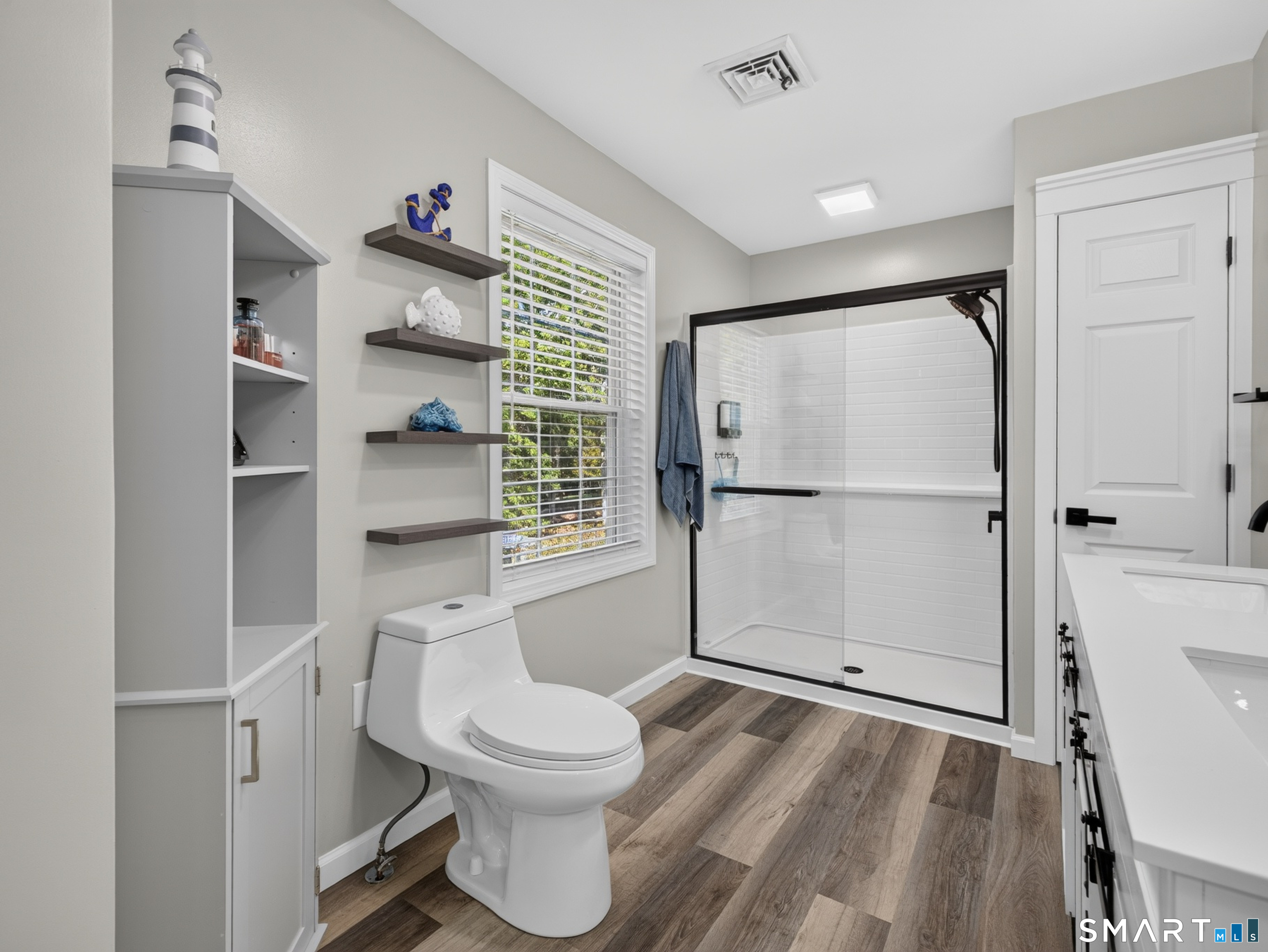 Bathroom with a black-framed glass shower, white vanity, and wood-look flooring.