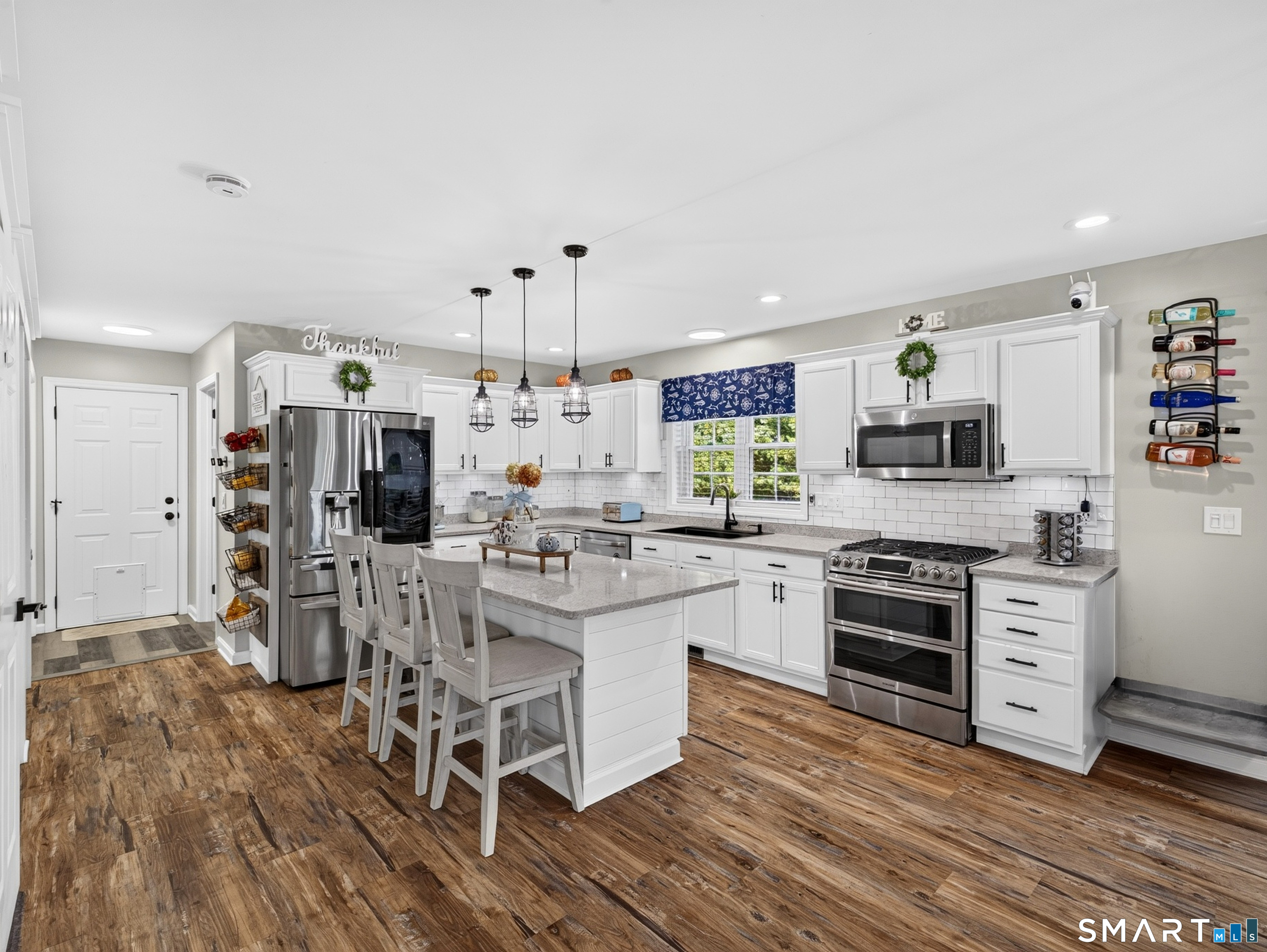 Bright white kitchen with a large island, stainless steel appliances, and wood-look flooring.
