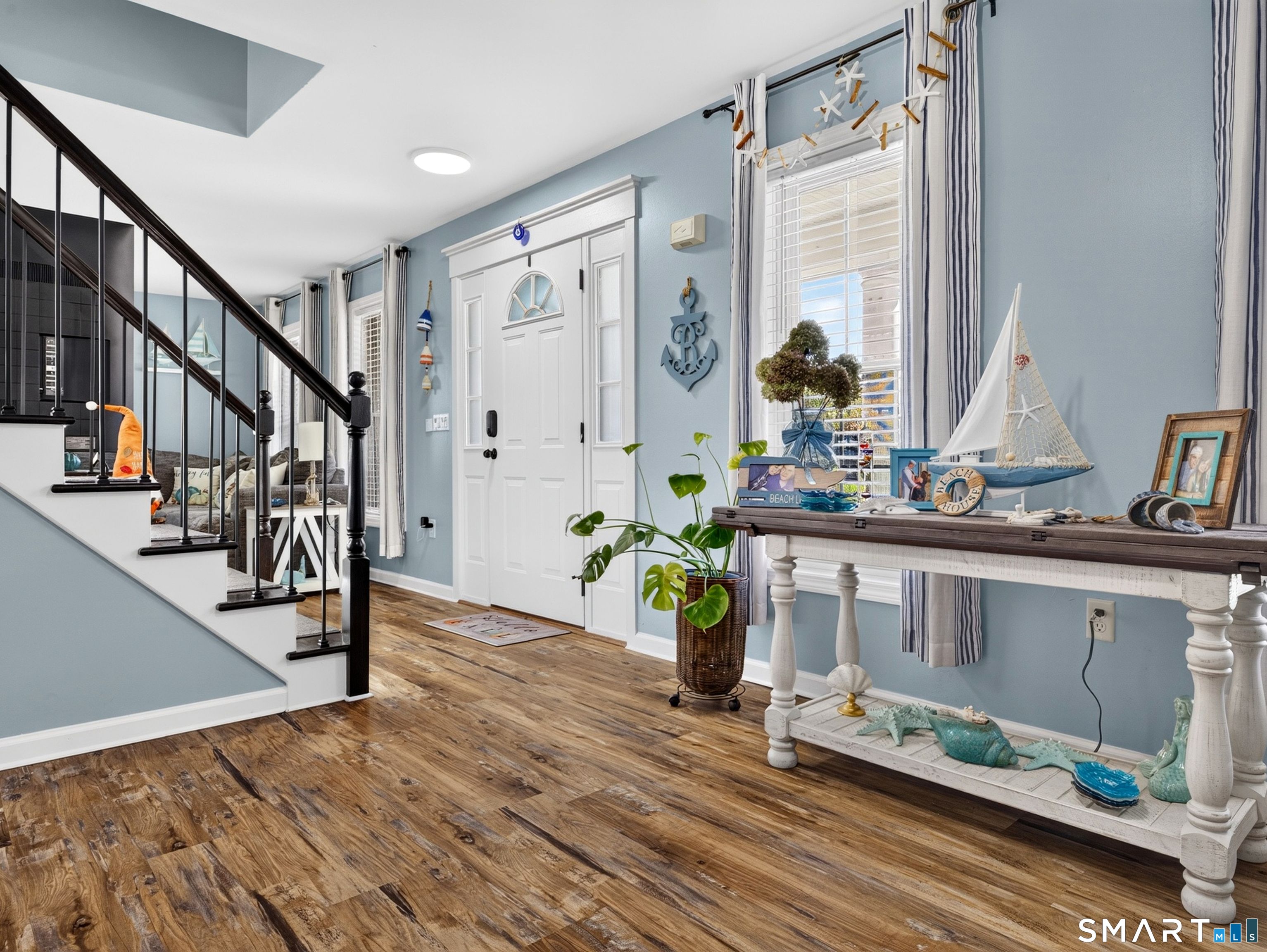 Coastal-style entryway with a white front door, staircase, and nautical decor on a console table.
