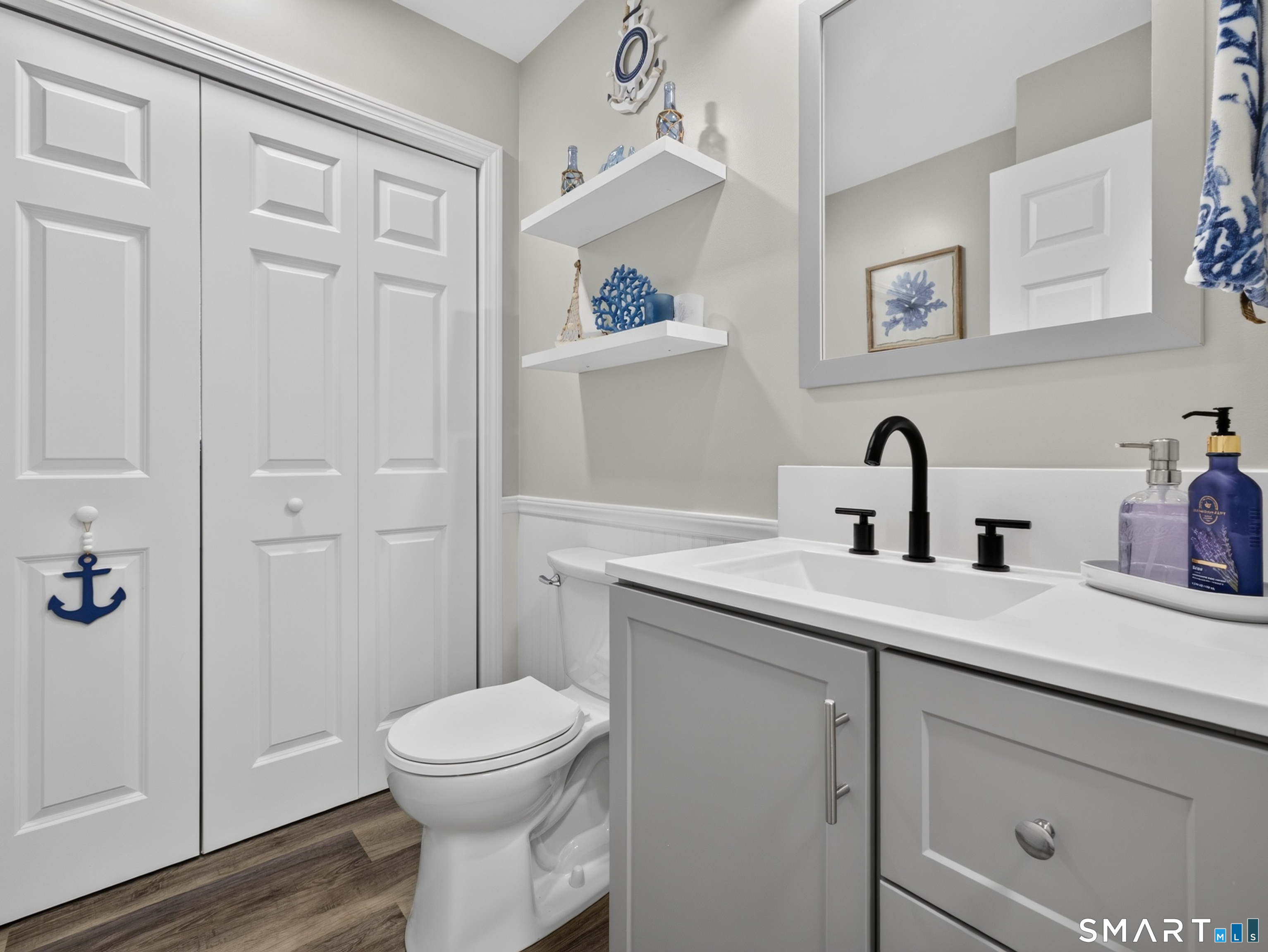 Bathroom with a gray vanity, black faucet, white toilet, and paneled closet doors.