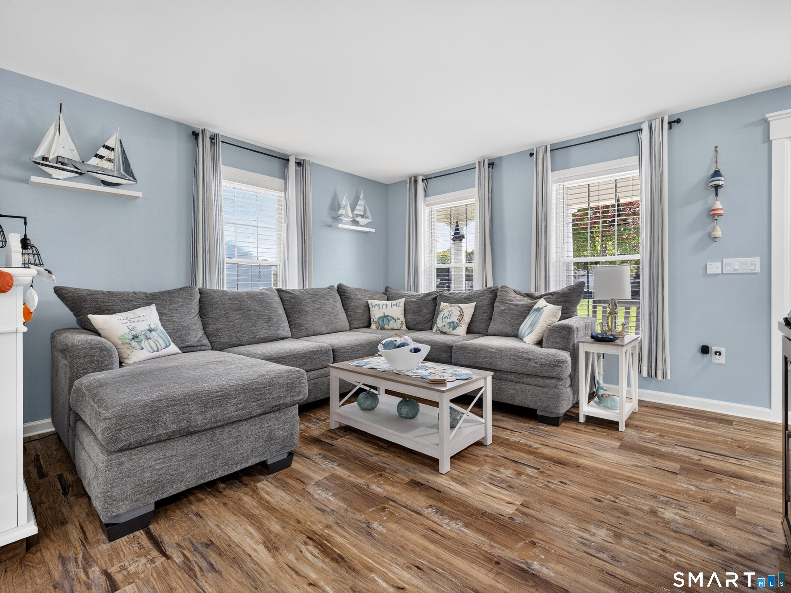 Living room with a gray sectional, blue walls, nautical decor, and wide-plank wood flooring.