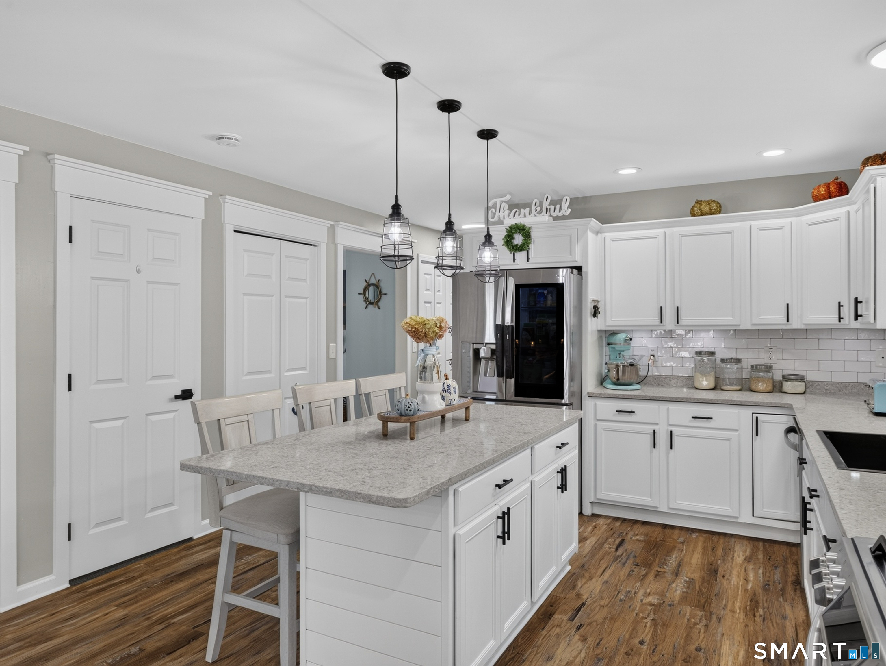 Bright kitchen with white cabinetry, a large island, stainless steel refrigerator, and wood flooring.