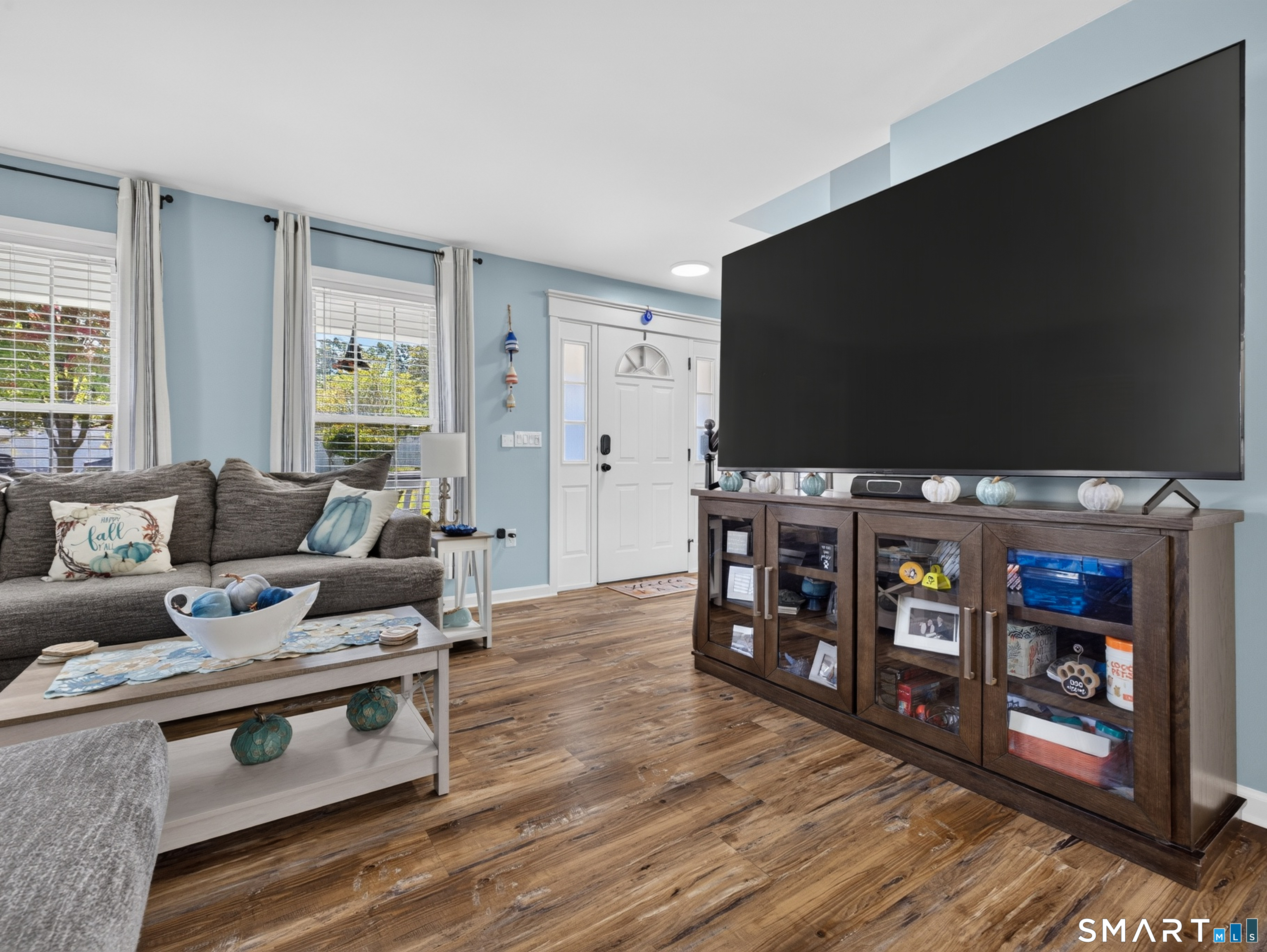 Living room with a large television, gray sectional, and wood-look flooring.