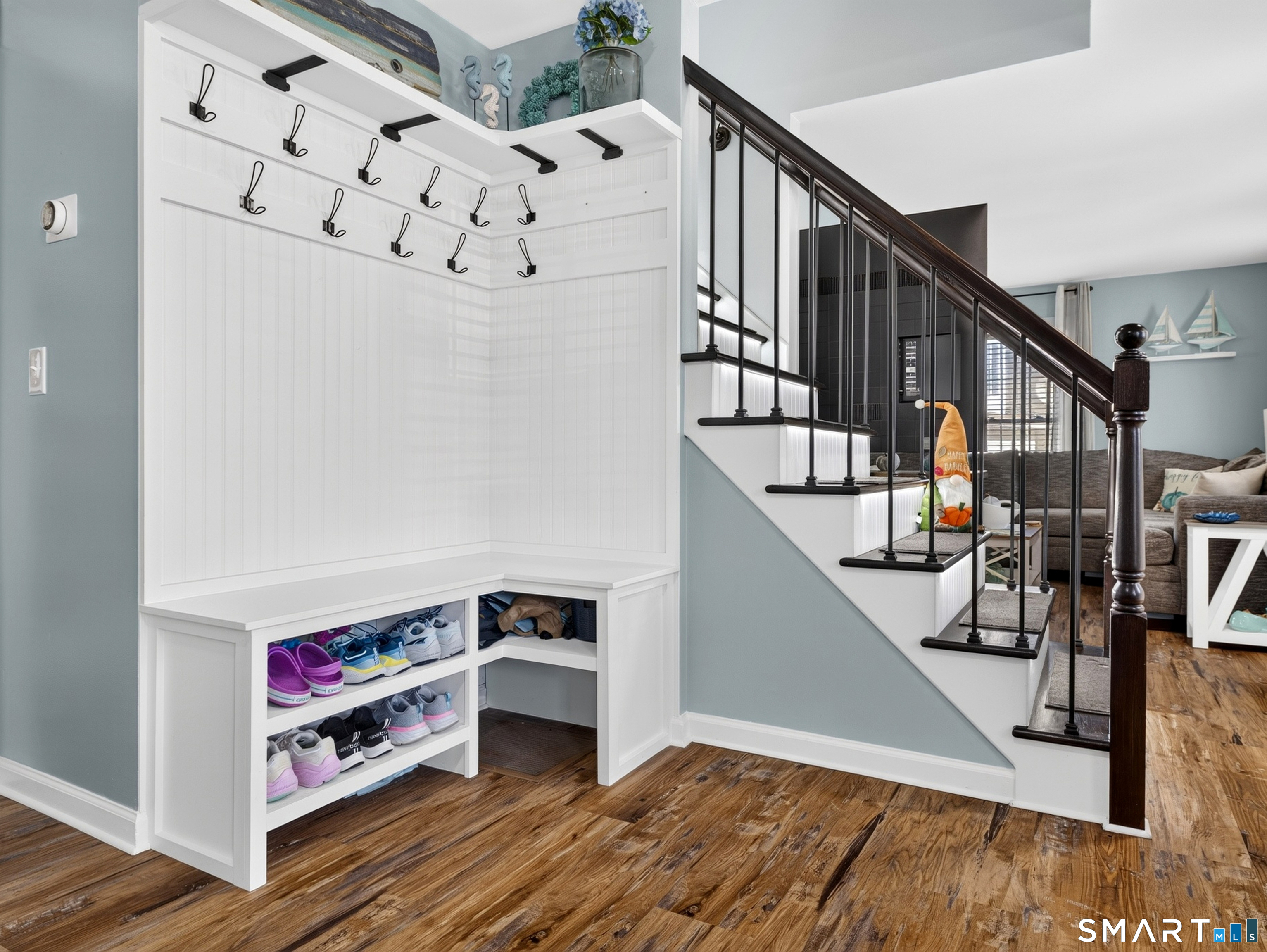 Entryway with built-in coat hooks and shoe shelves beside a staircase with dark wood railing.
