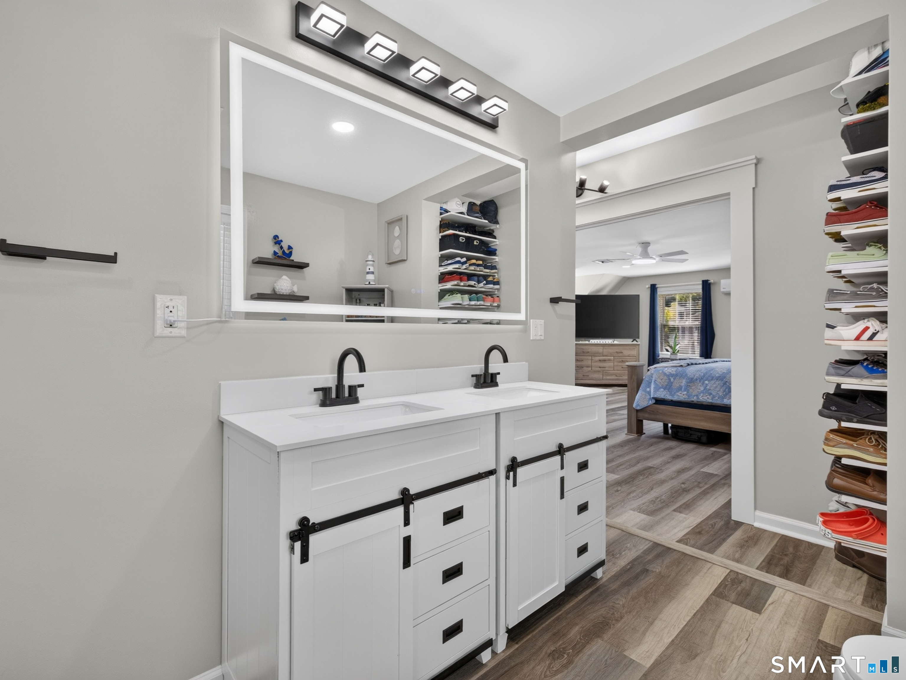 Bathroom with a white double vanity and black fixtures, opening onto a furnished bedroom.