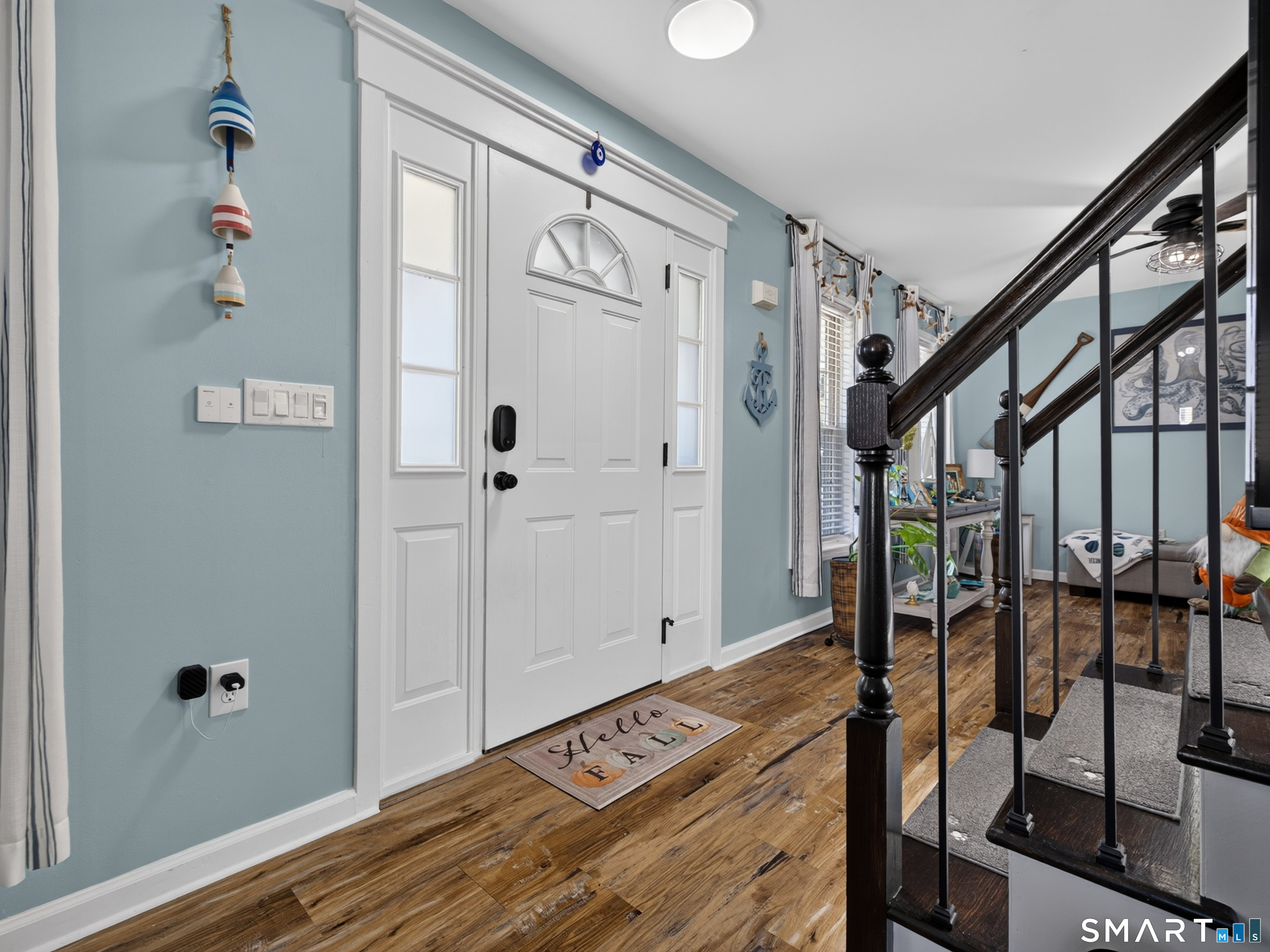 Entry foyer with a white front door, blue walls, wood flooring, and a dark staircase.