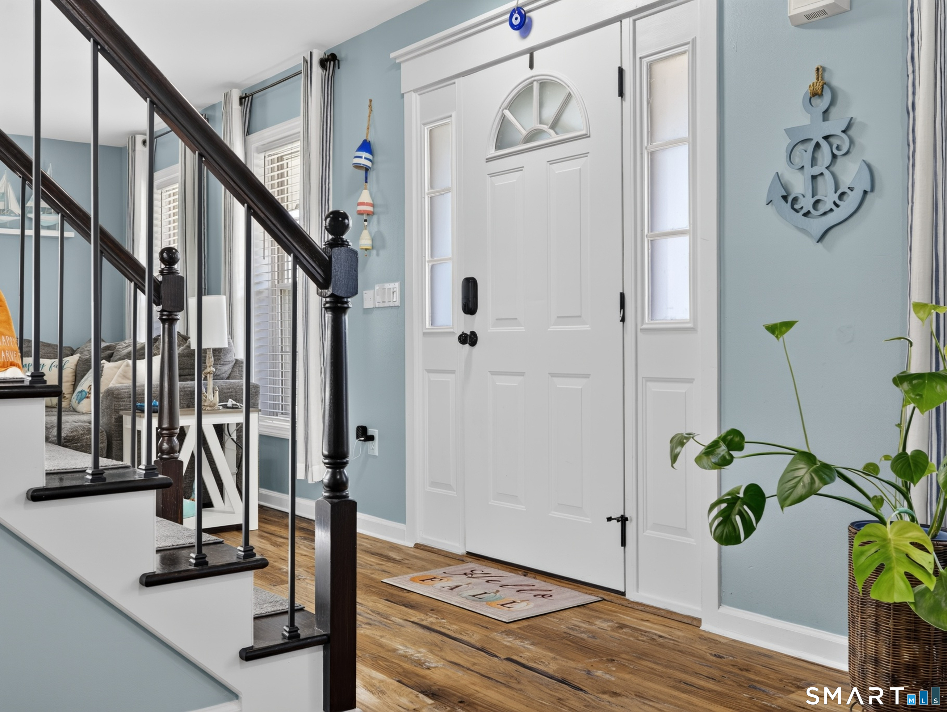 Entryway with a white glass-paneled front door, dark staircase, wood flooring, and coastal decor.