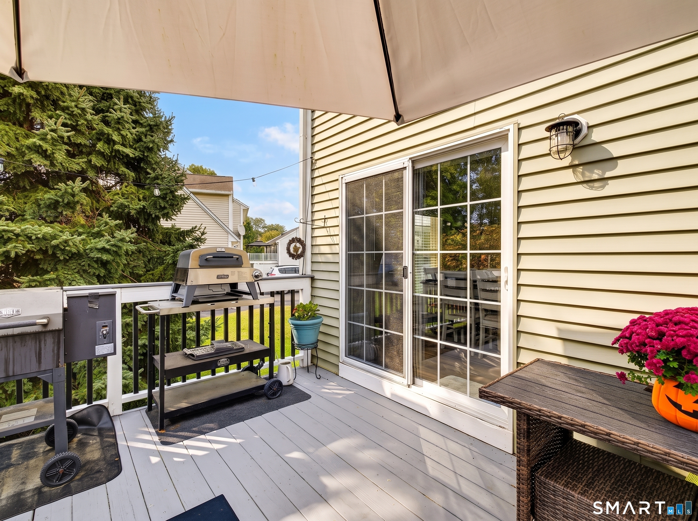 Deck with a barbecue grill, patio table, and sliding glass doors beneath a large umbrella.