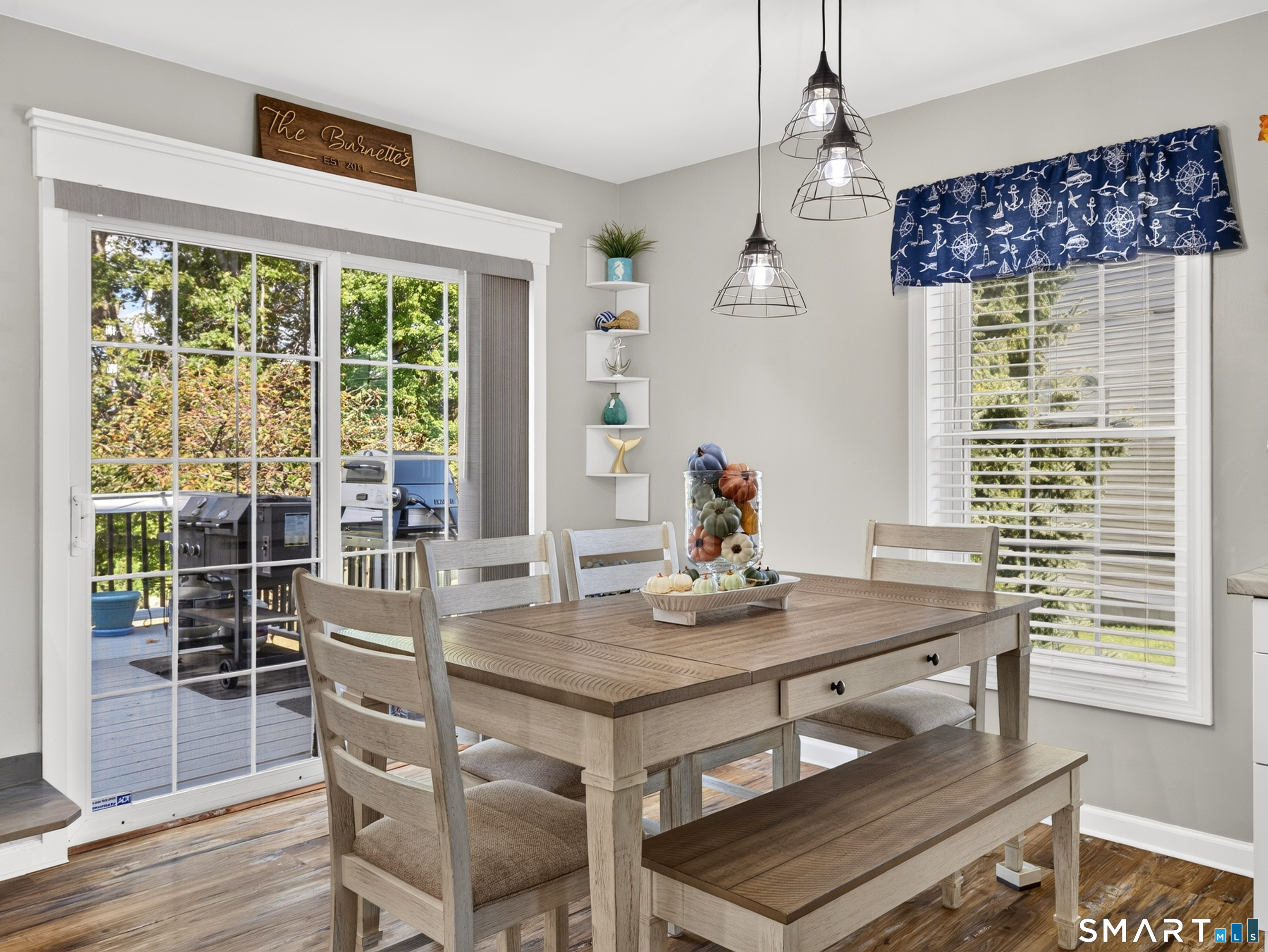 Dining room with a wood table and bench beside sliding doors opening to a deck and grill.