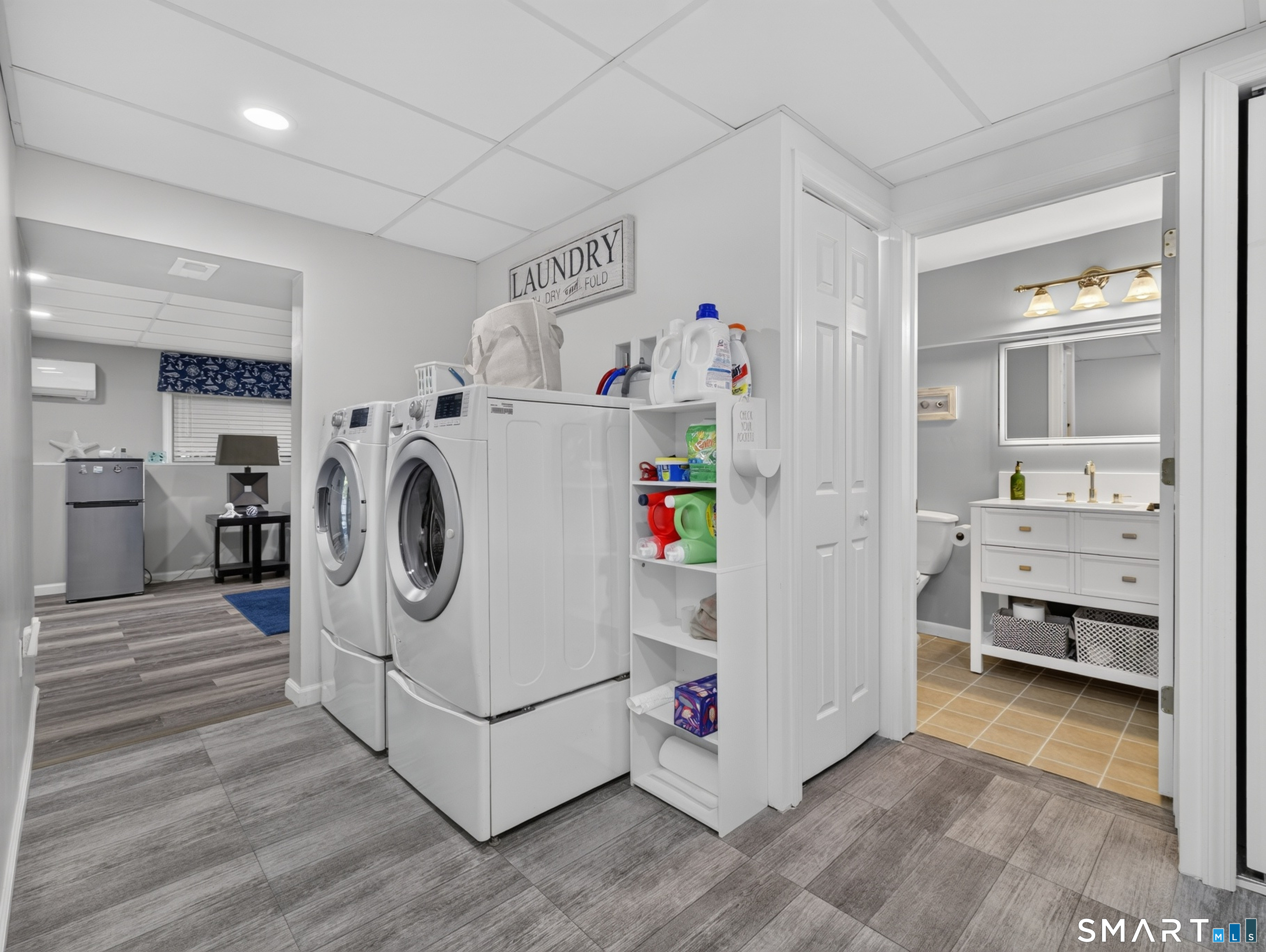 Laundry room with side-by-side washer and dryer, open shelving, and an adjoining bathroom.