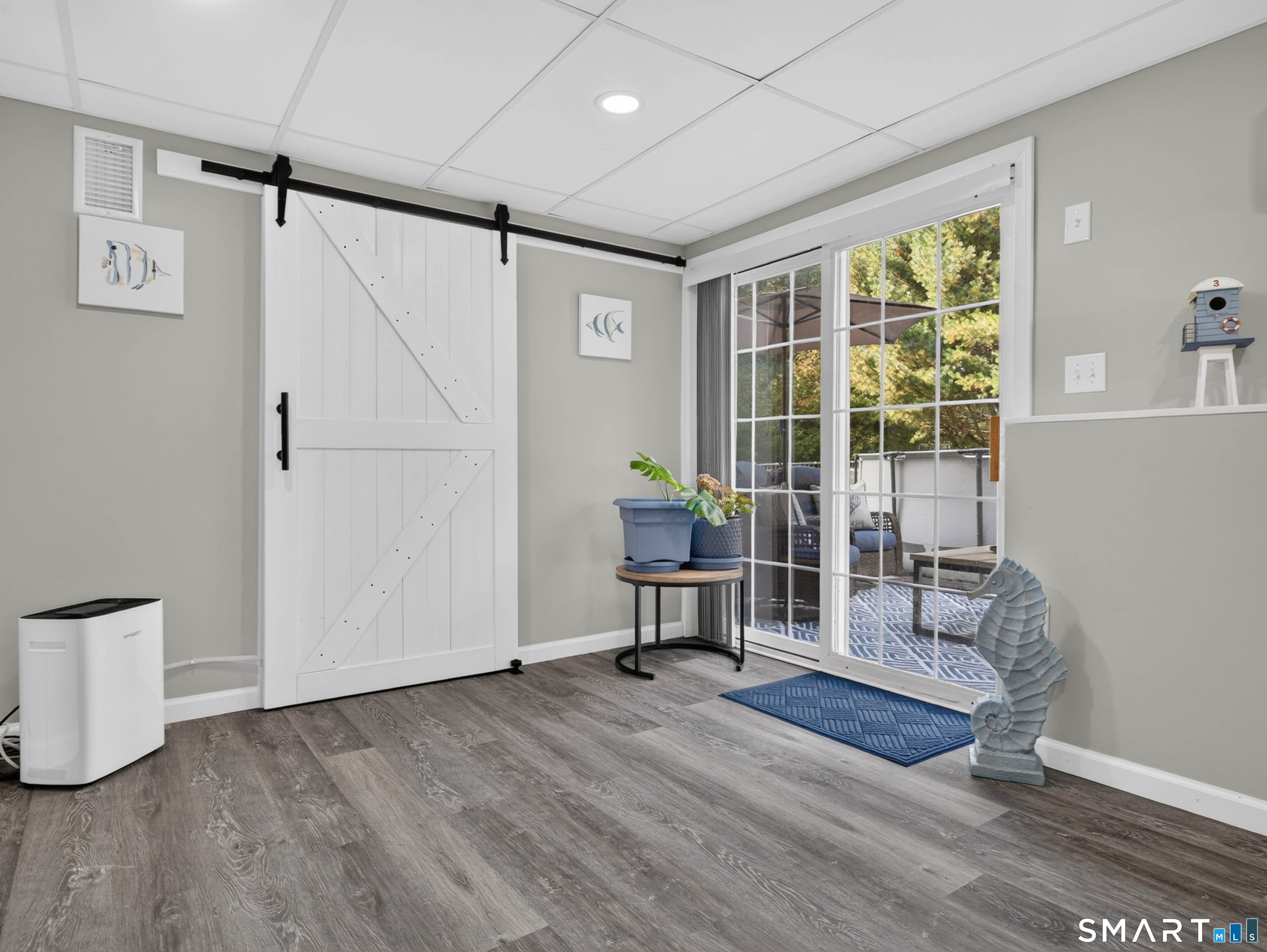 Bright room with a white sliding barn door, gray wood-look flooring, and glass doors opening to a furnished patio.