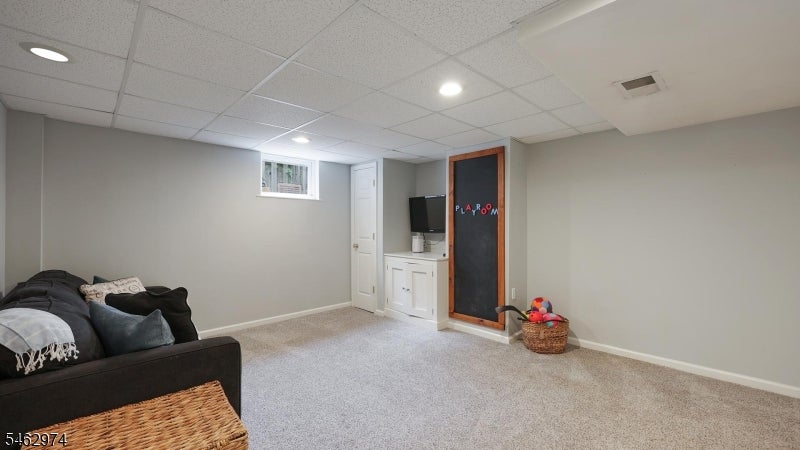 Basement recreation room with a dark sectional, beige carpet, white cabinetry, and a chalkboard playroom door.