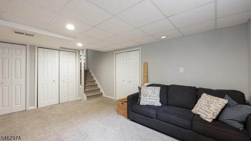 Furnished basement family room with a dark sofa, carpet, multiple closets, and stairs.