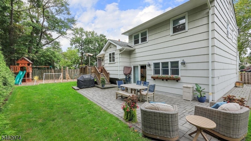 Back of a gray-sided house with a furnished patio, lawn, and children's playset.